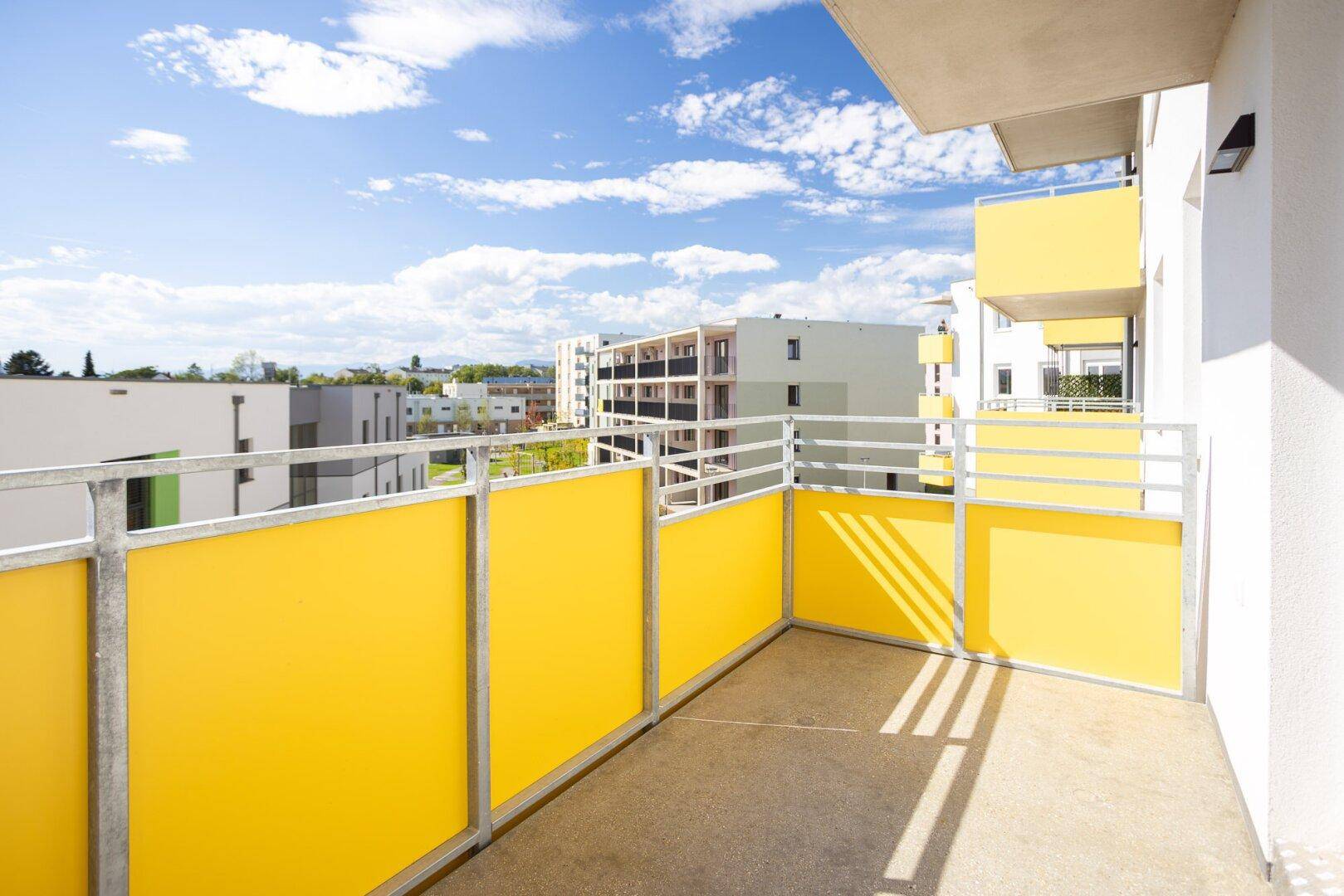 Heller Balkon mit gelben Sichtschutzelementen und Blick auf die moderne Wohnanlage.