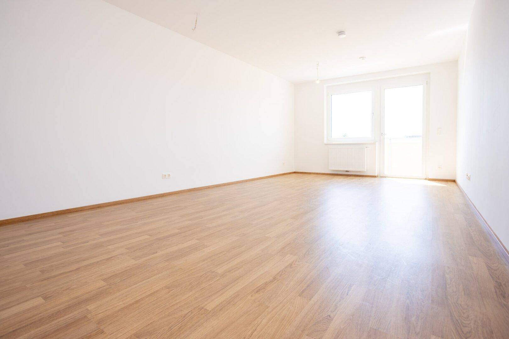 Helles, leeres Zimmer mit modernem Laminatboden und weiß gestrichenen Wänden, bereit zur Einrichtung.