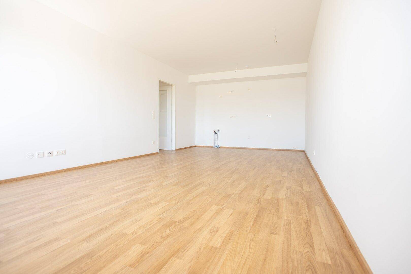 Leerer Küchenraum mit Laminatboden und Anschlüssen für eine Einbauküche, bereit zur Gestaltung.