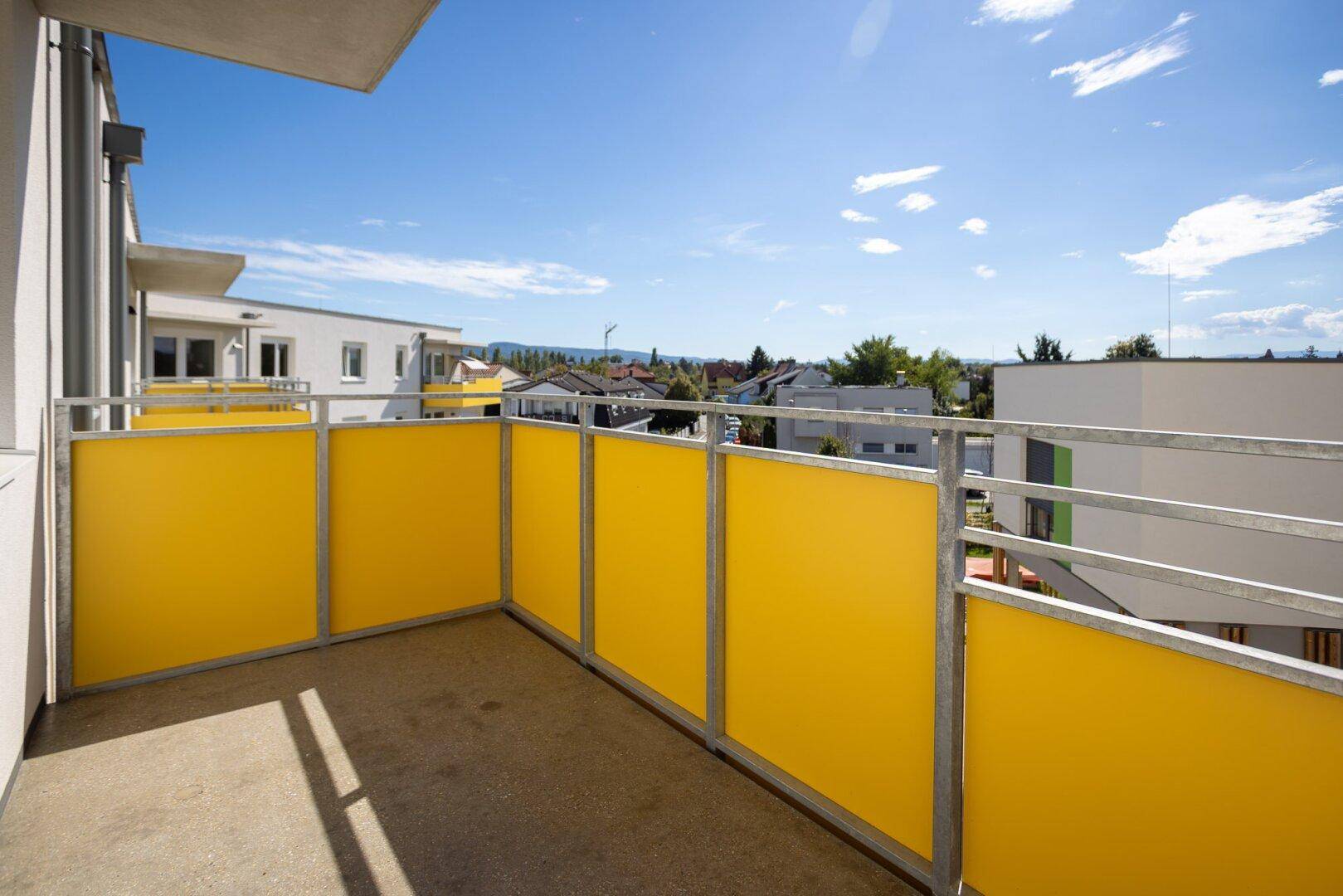 Sonniger Balkon mit gelben Brüstungselementen und weitem Blick über die Umgebung.