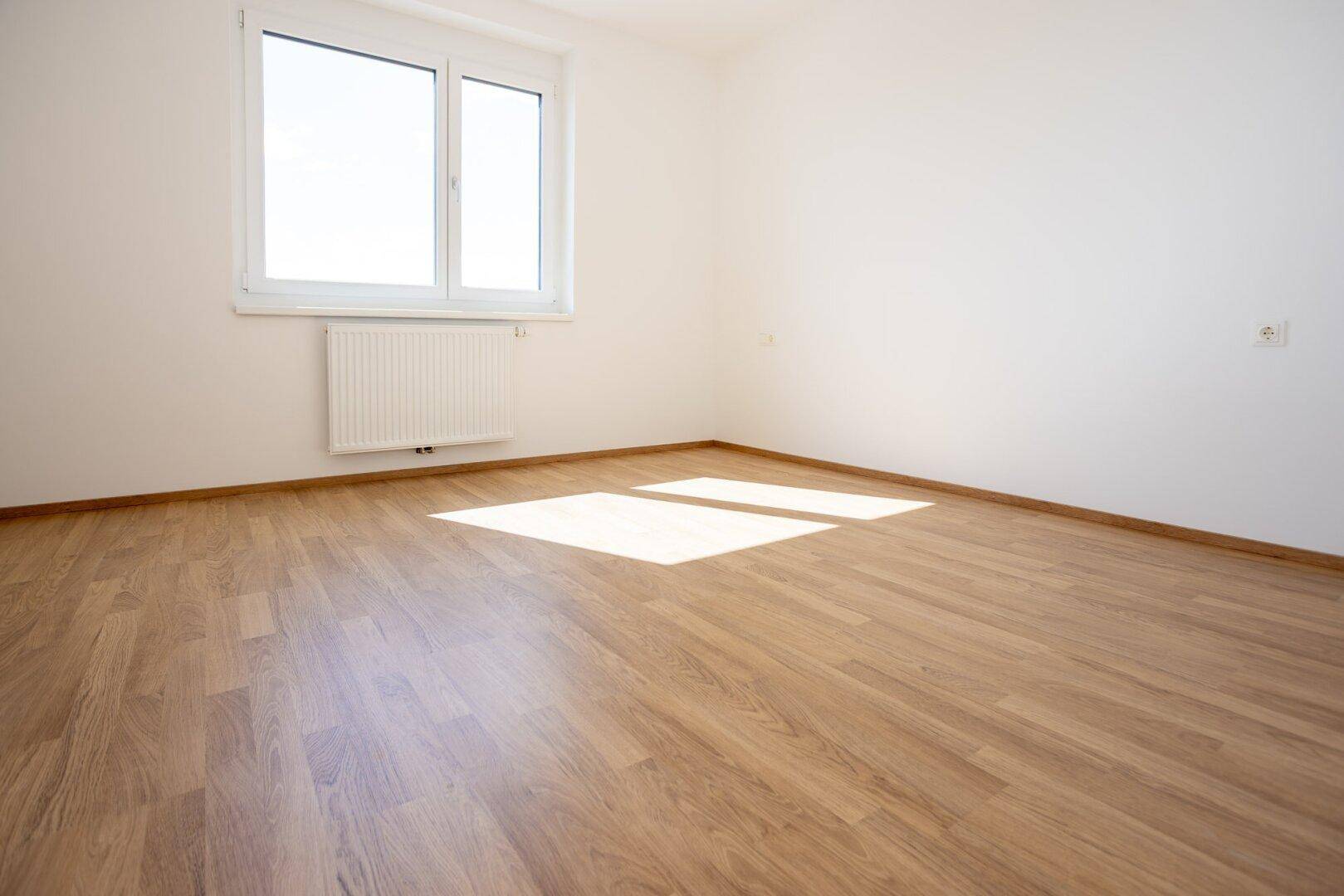 Helles Schlafzimmer mit Laminatboden und großem Fenster, das viel natürliches Licht hereinlässt.