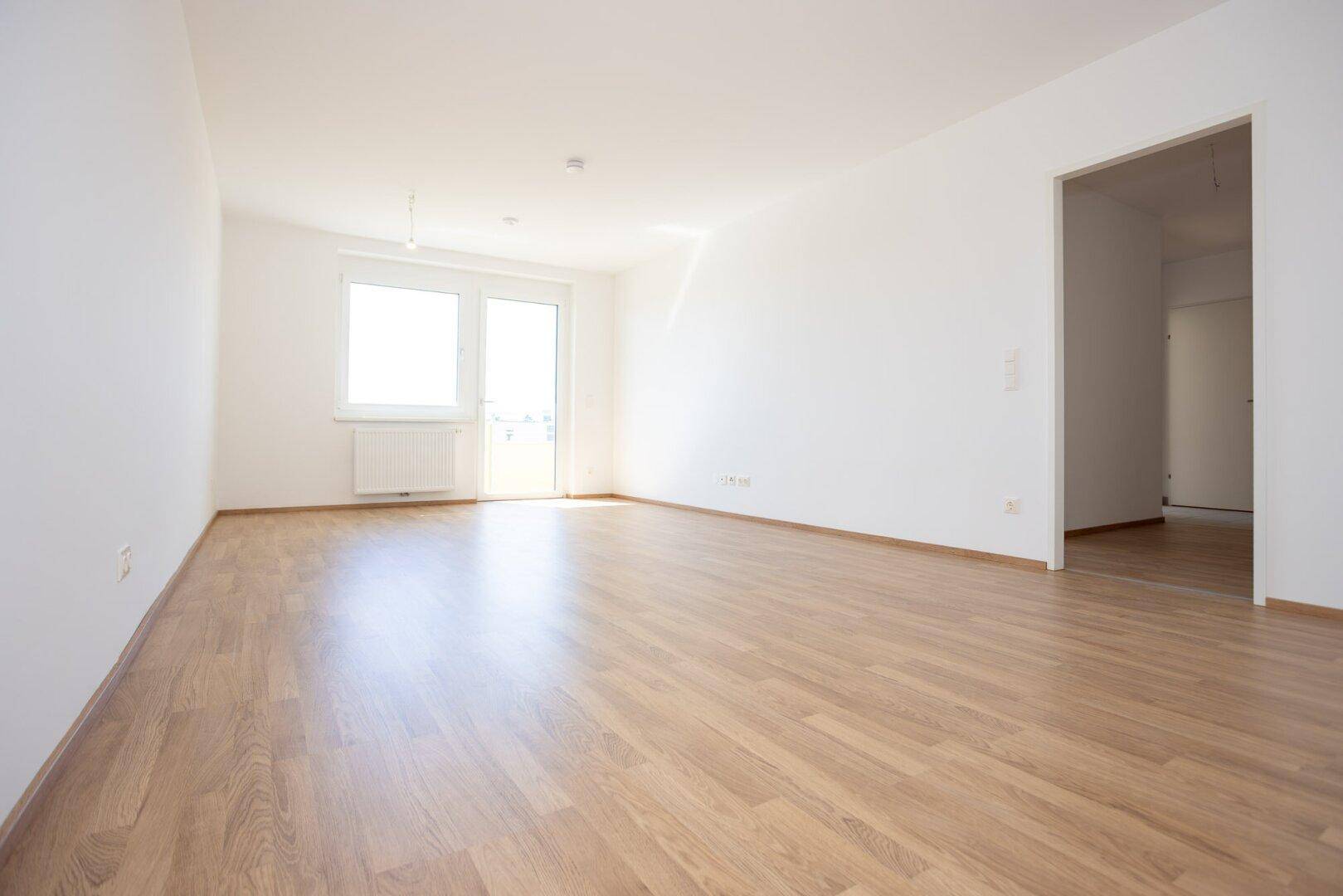 Geräumiges, helles Zimmer mit Laminatboden und Zugang zu einem weiteren Raum, ideal für Wohnzwecke.