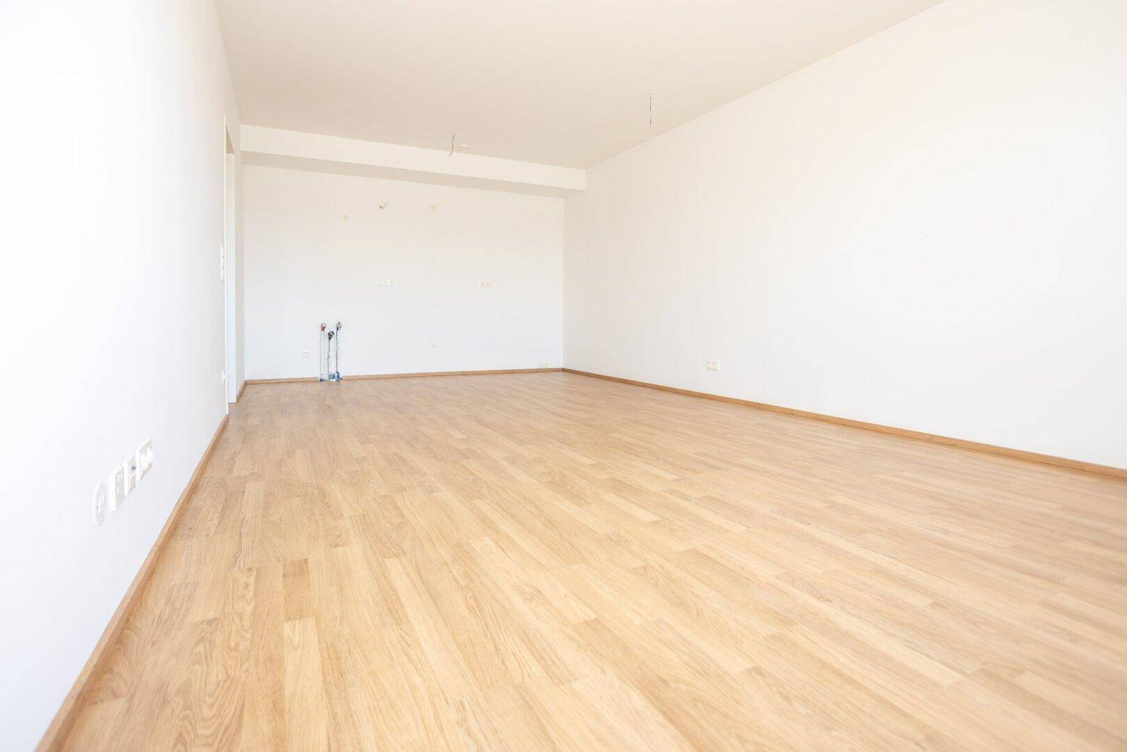 Geräumiger Küchenbereich mit Laminatboden und vorbereiteten Anschlüssen für die Kücheninstallation.