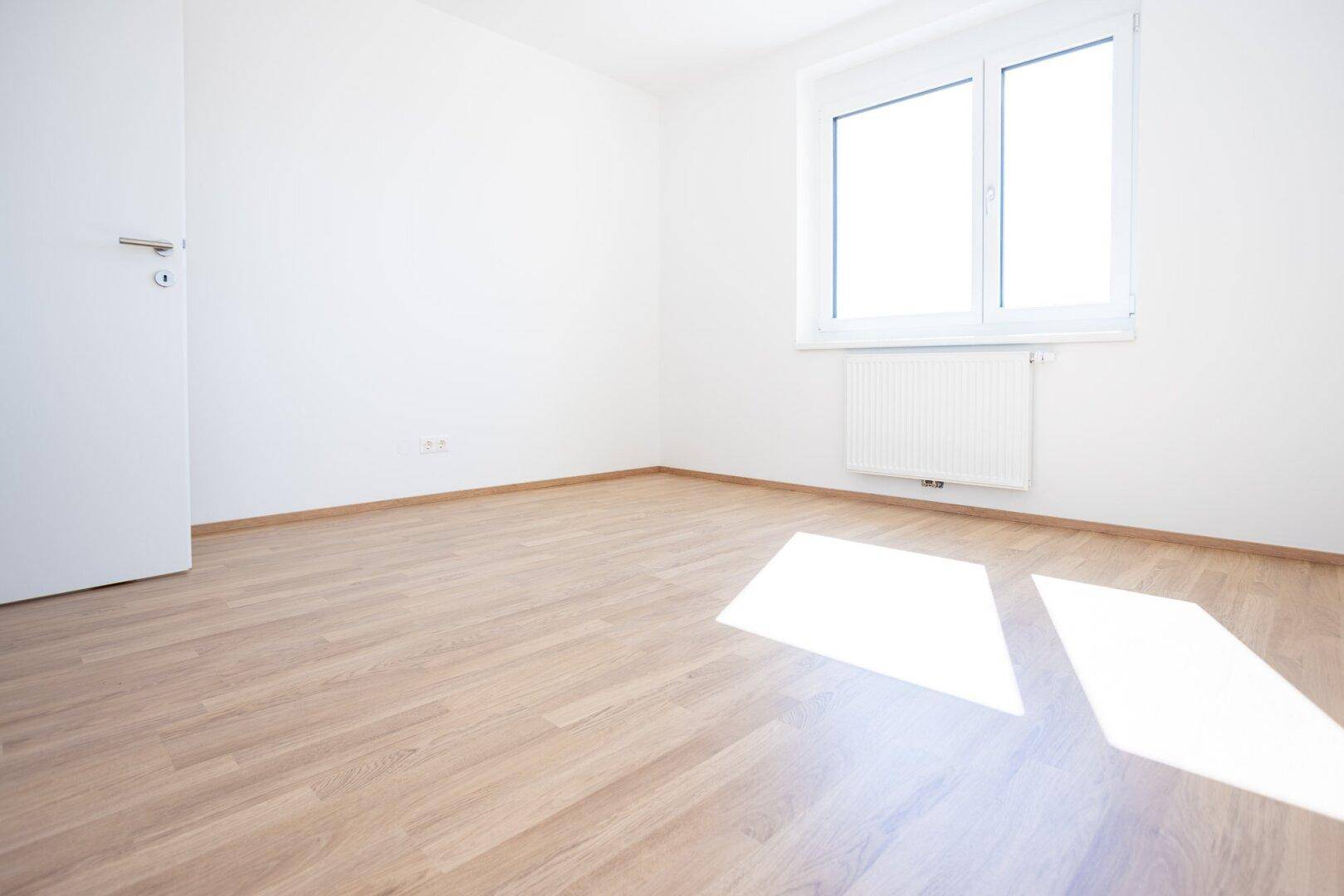 Freundliches Schlafzimmer mit Laminatboden, weiß gestrichenen Wänden und einer Tür, die zu einem anderen Raum führt.