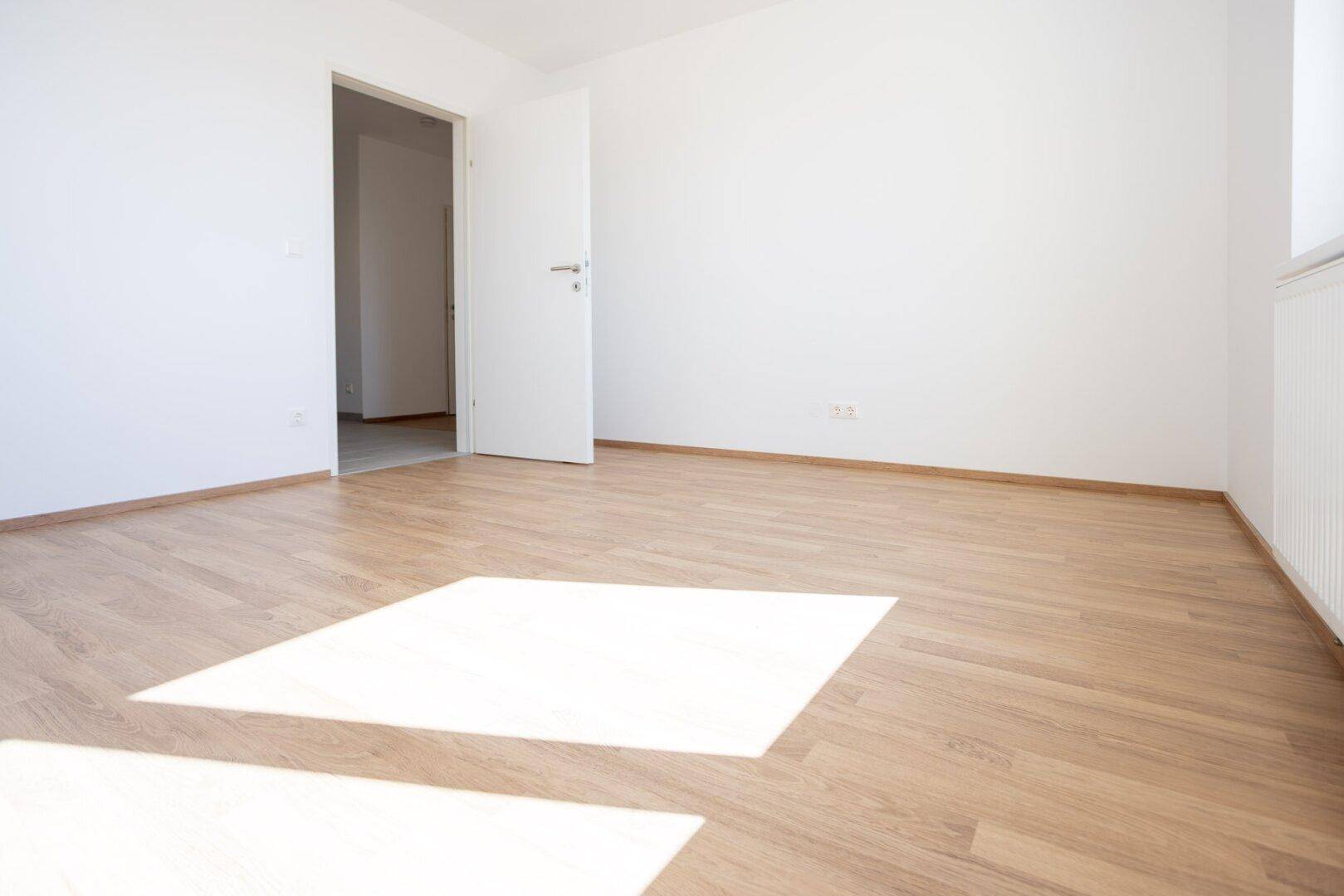 Sonniger Raum mit Laminatboden und weiß gestrichenen Wänden, ideal als Schlaf- oder Kinderzimmer.