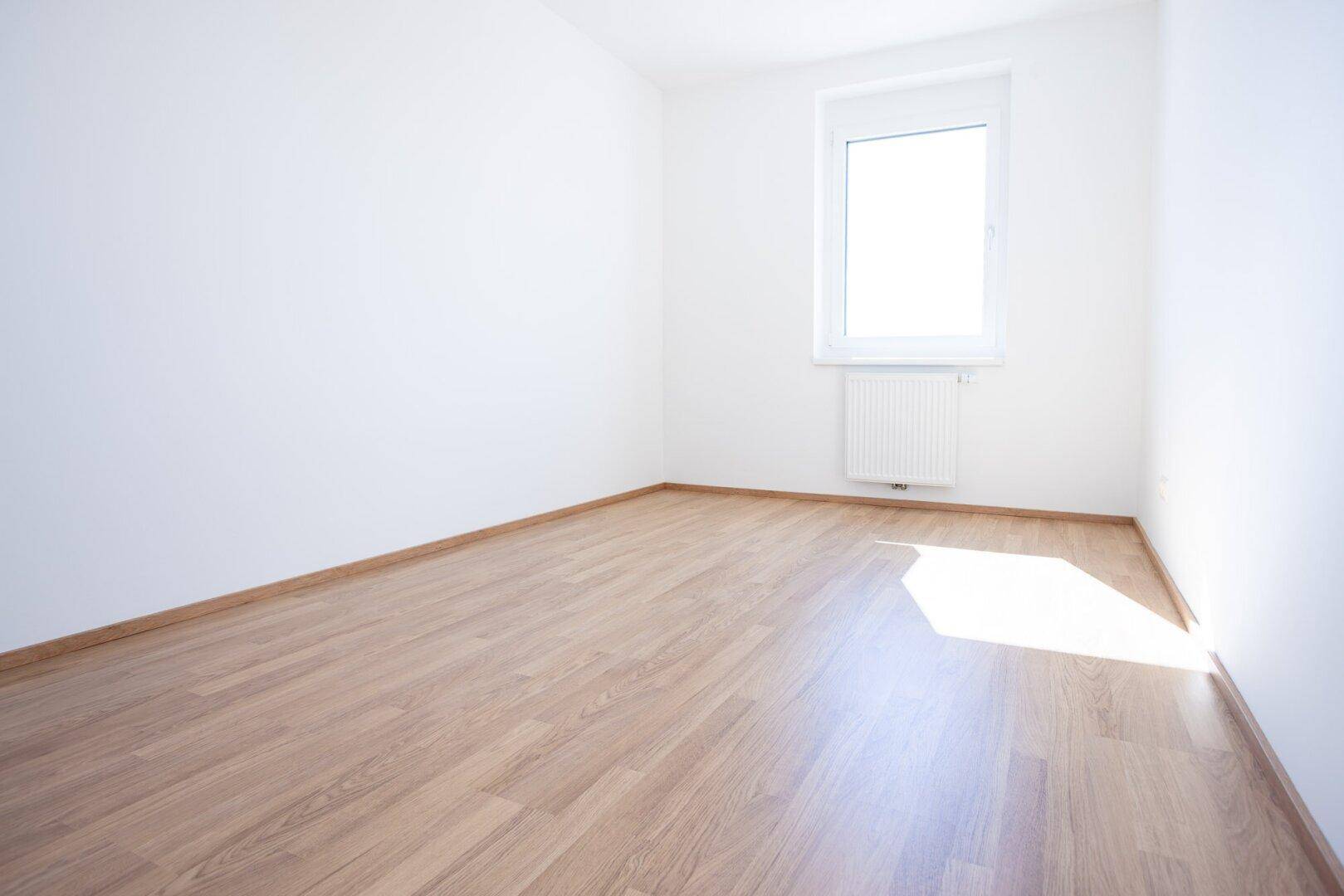 Freundliches Zimmer mit Laminatboden und weiß gestrichenen Wänden, bereit für individuelle Gestaltung.