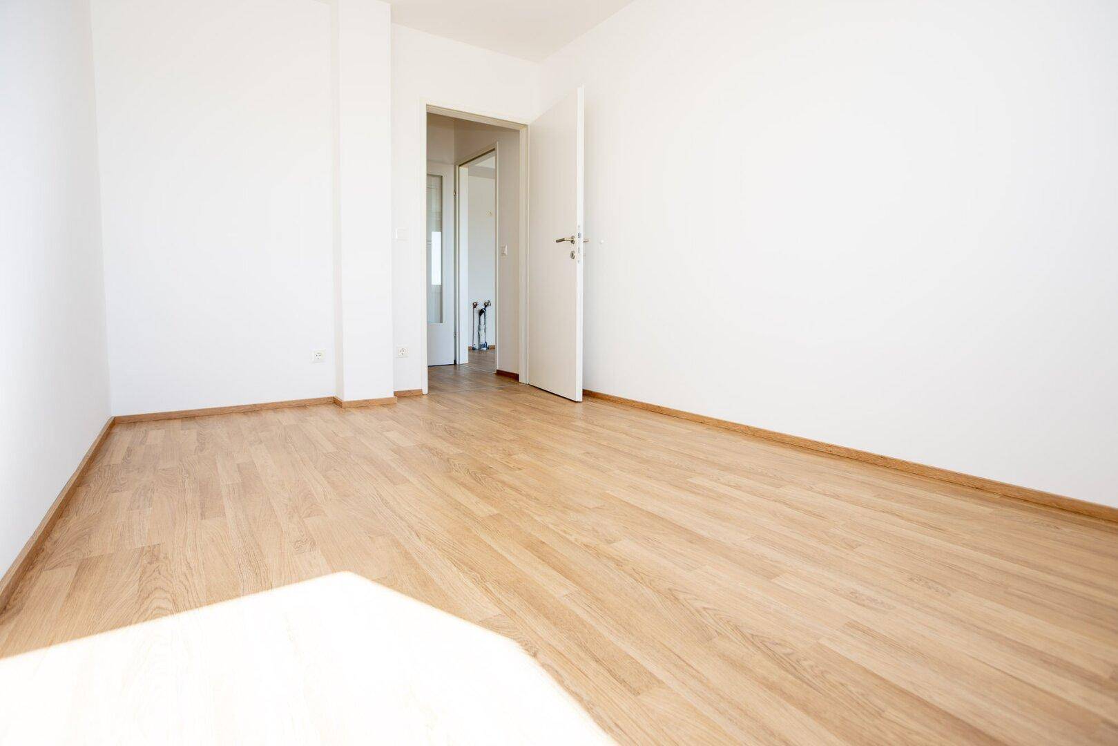 Geräumiges Zimmer mit Laminatboden und offenem Zugang zu einem weiteren hellen Raum.