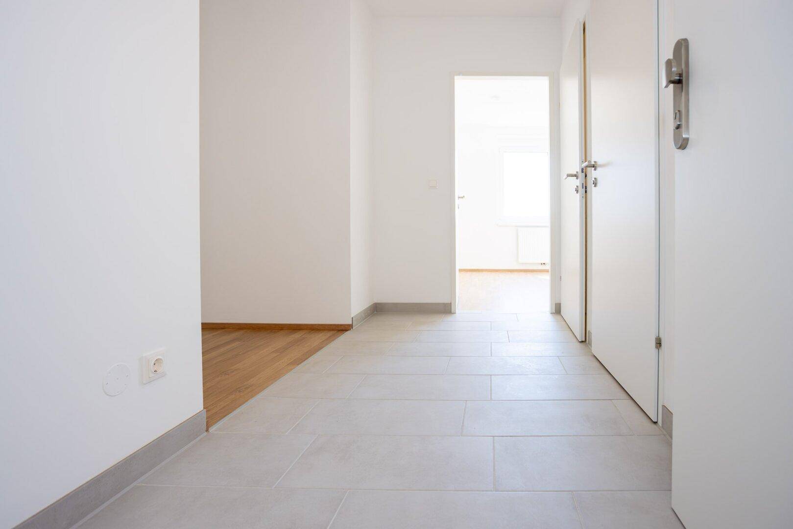 Heller Flur mit modernen grauen Bodenfliesen und Zugang zu weiteren Räumen der Wohnung.