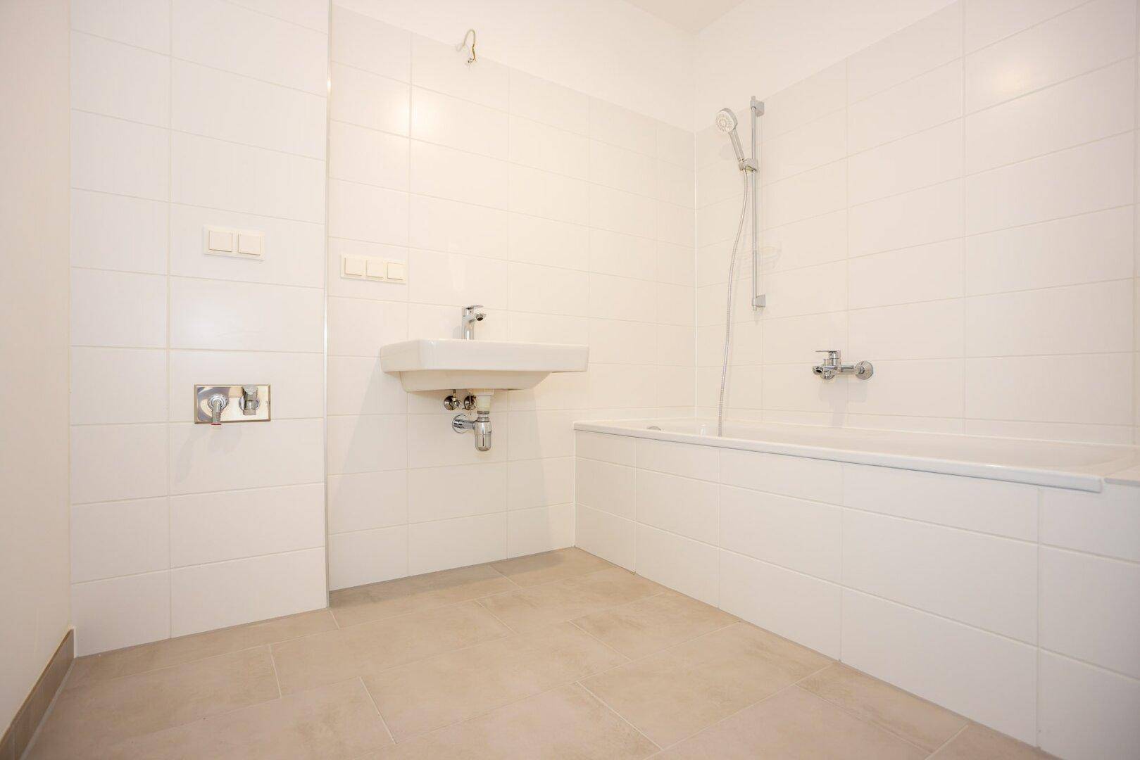 Modernes Badezimmer mit weißen Wandfliesen, Badewanne mit Duschfunktion und einem Waschbecken.