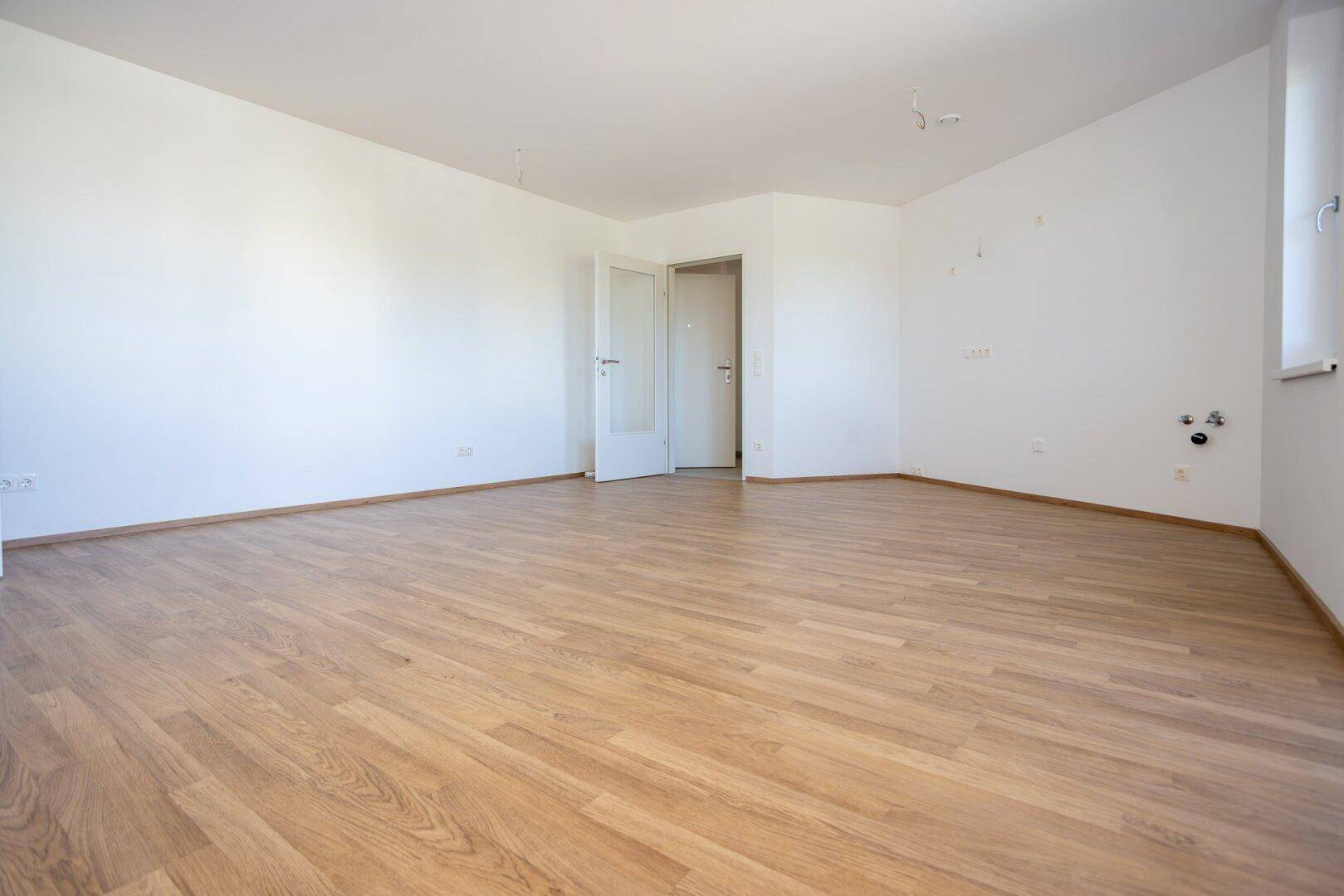 Geräumiger, leerer Raum mit hellem Laminatboden und weißen Wänden, bereit zur individuellen Gestaltung.