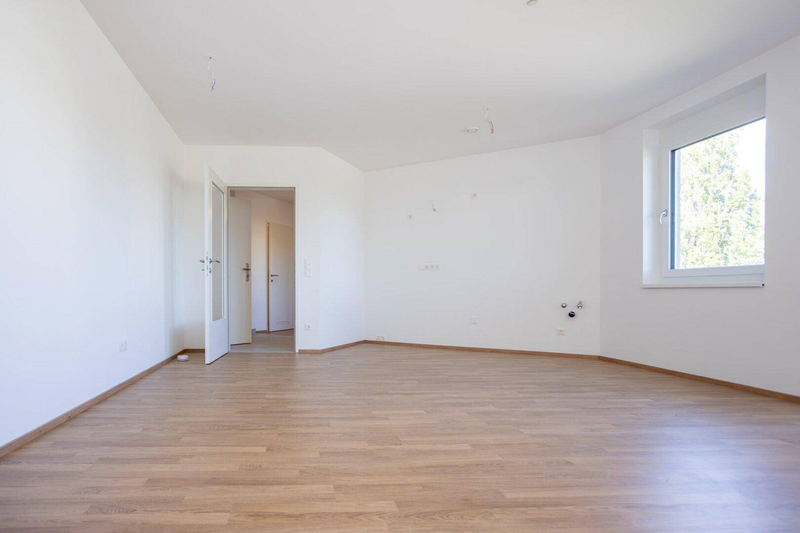 Geräumiger, unmöblierter Raum mit hellem Laminatboden und weißen Wänden, ideal für individuelle Gestaltung.