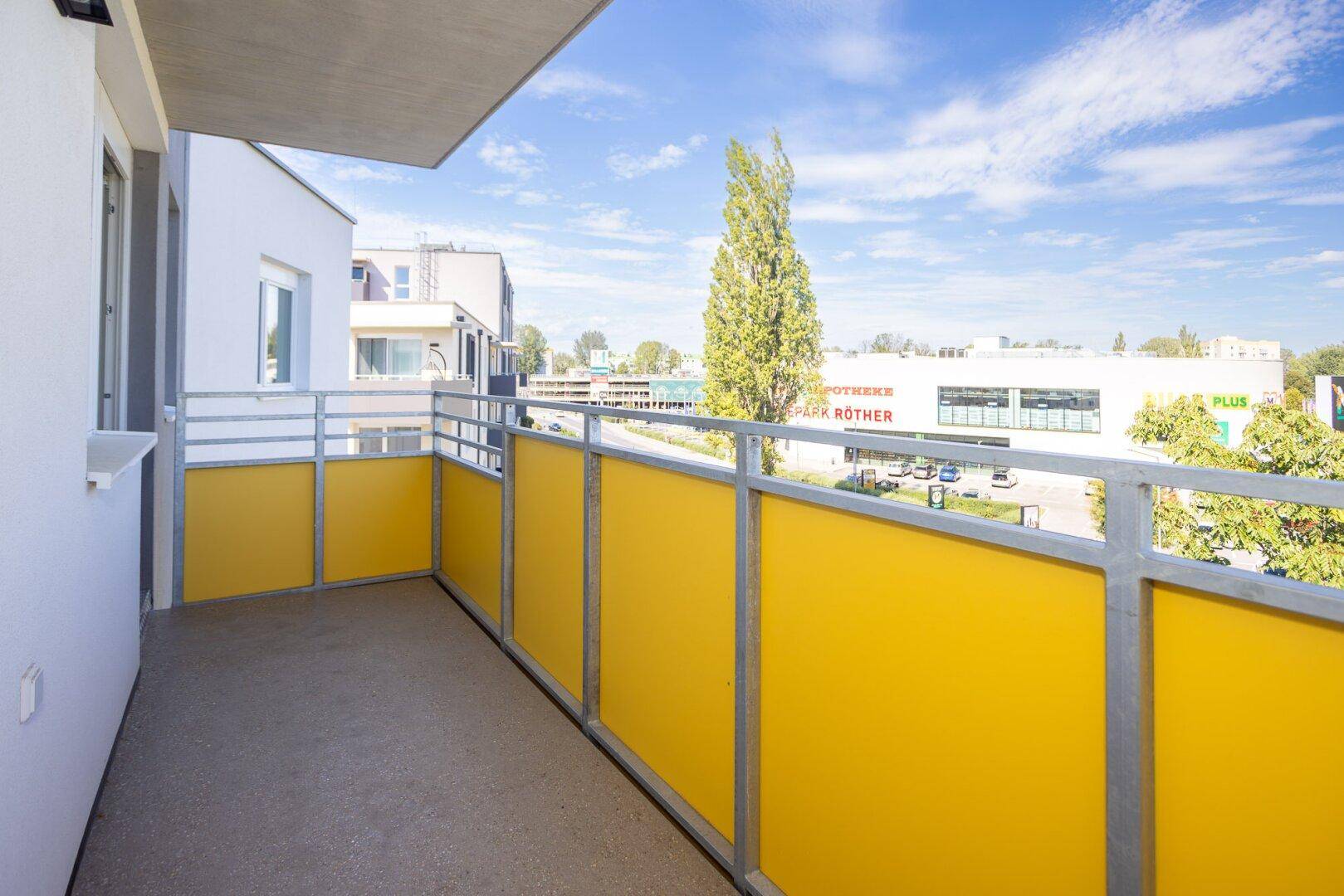 Moderner Balkon mit gelben Brüstungselementen und Blick auf die belebte Straße und Geschäfte.