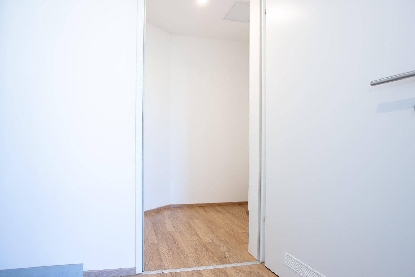 Heller Flur mit weiß gestrichenen Wänden und Zugang zu einem weiteren Zimmer mit Laminatboden.