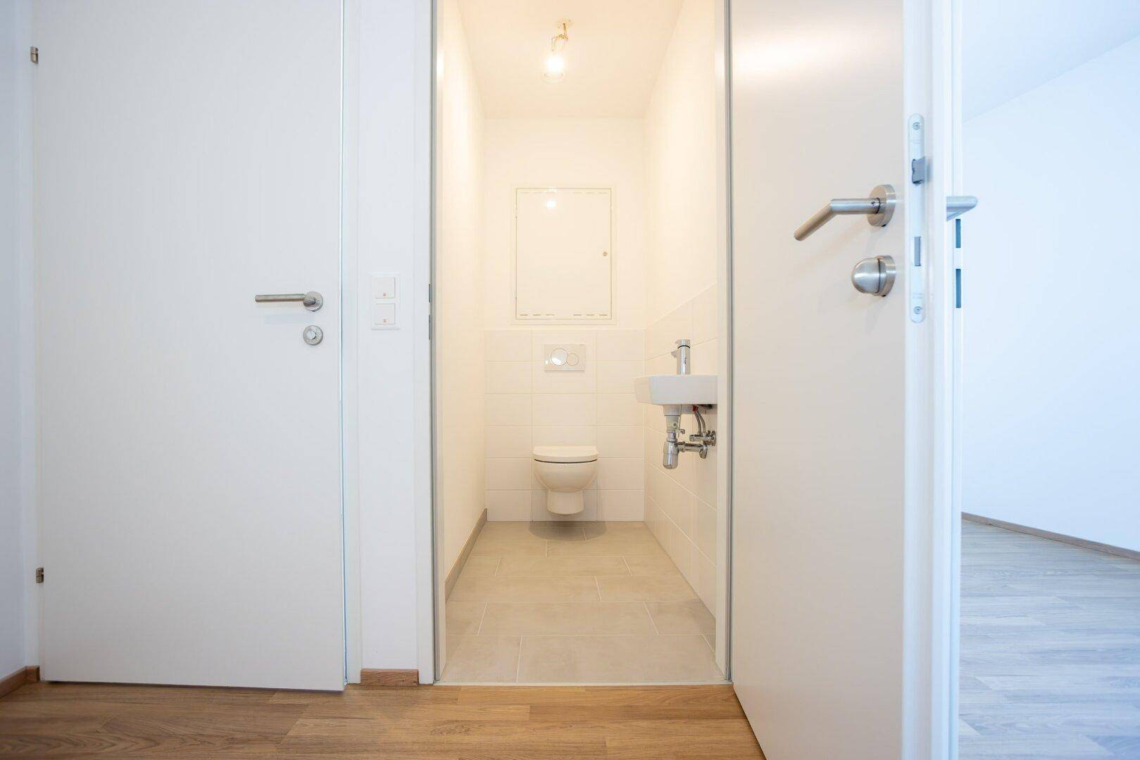 Kleines Gäste-WC mit weißen Fliesen, wandhängendem WC und einem kompakten Waschbecken.
