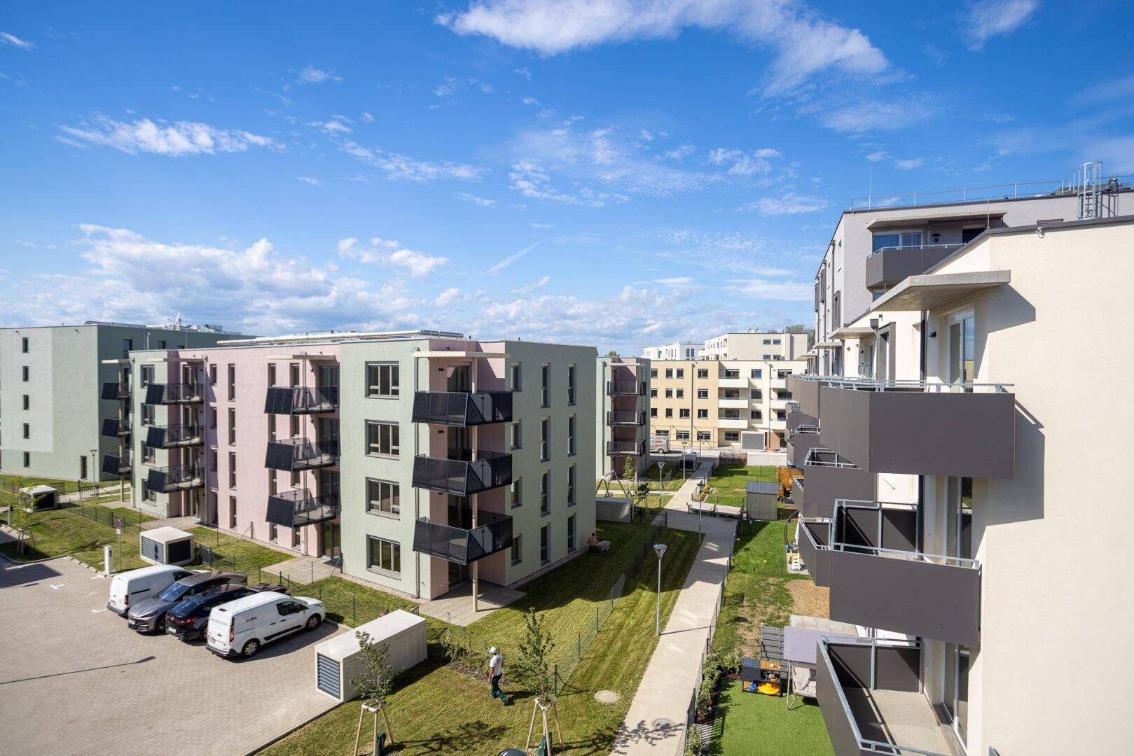 Panoramablick auf eine moderne Wohnsiedlung mit farbigen Gebäuden, Balkonen und angelegten Grünflächen.