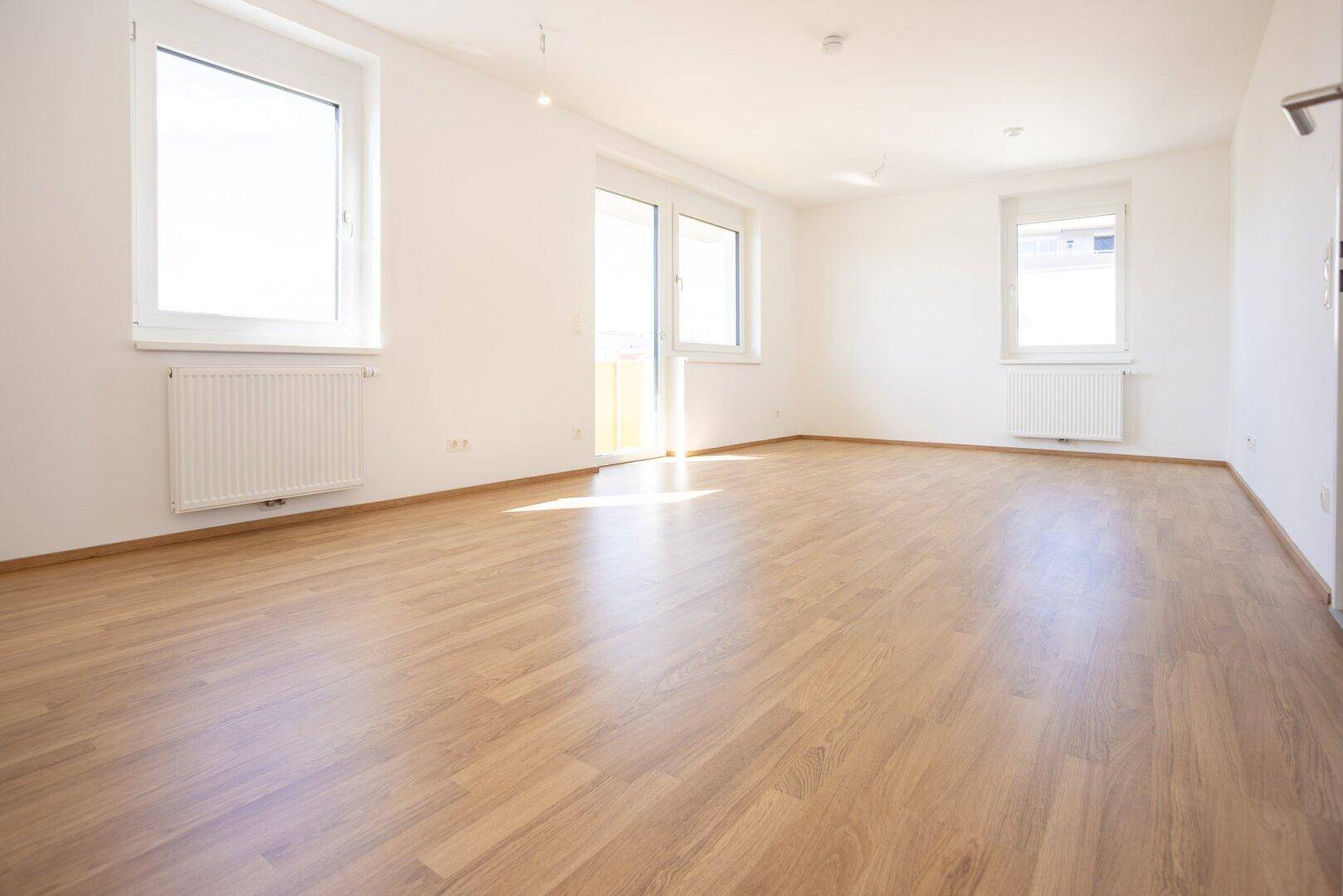 Lichtdurchfluteter Raum mit hellem Laminatboden, weißen Wänden und Zugang zum Außenbereich.