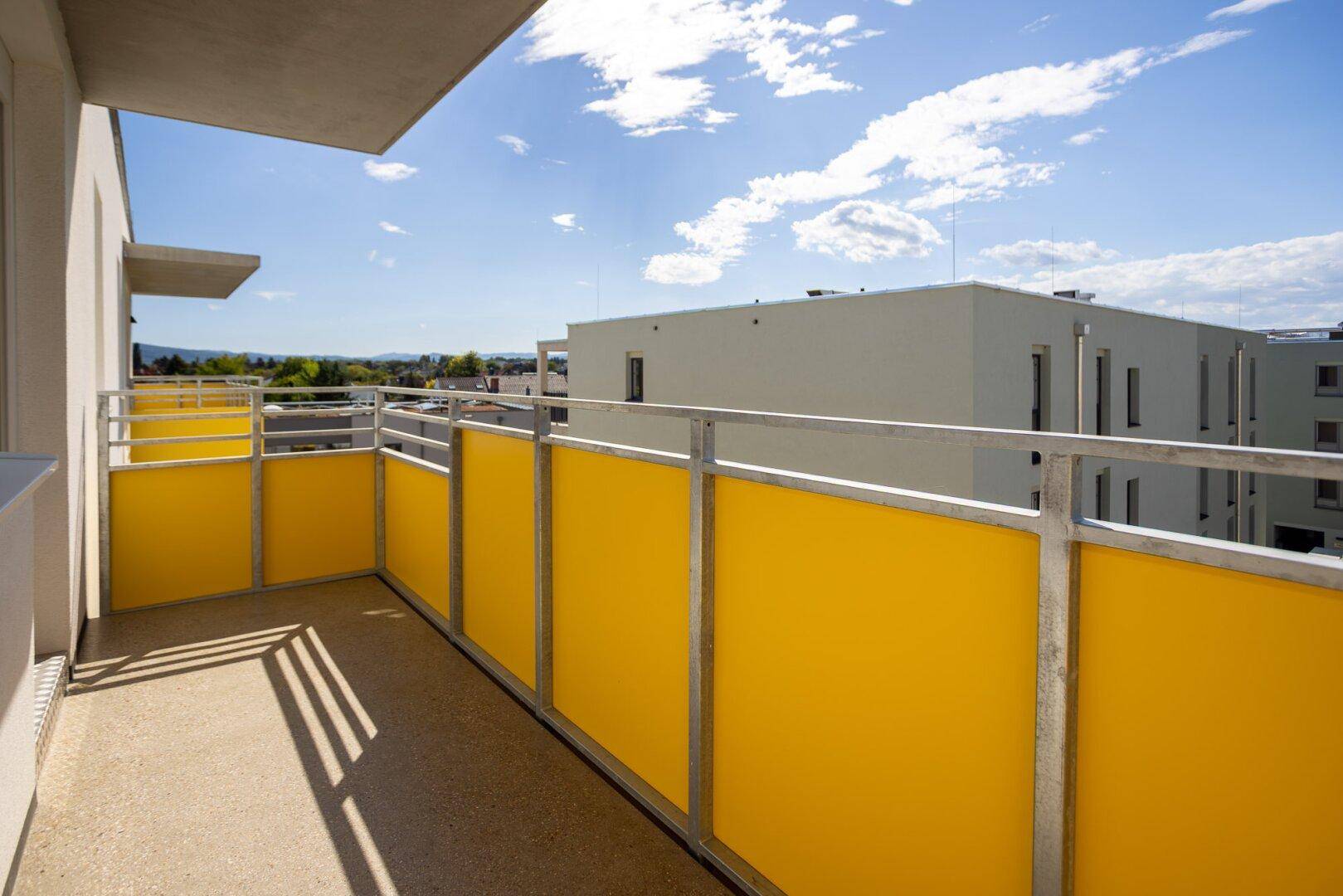 Geräumiger Balkon mit gelben Brüstungselementen und weitem Blick über die moderne Wohnanlage.