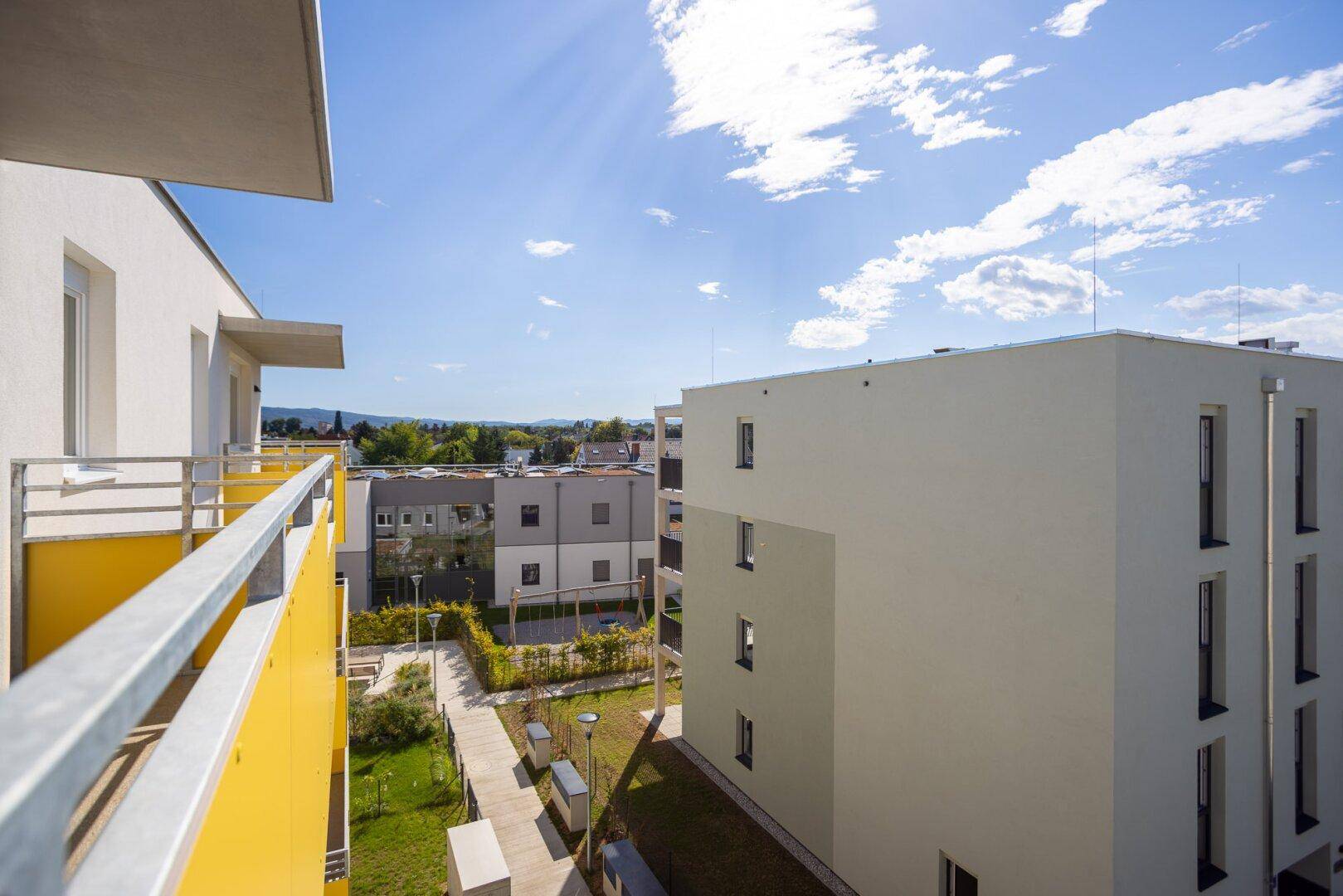 Weitblick vom Balkon über eine moderne Wohnsiedlung mit Grünflächen und Bergsilhouette im Hintergrund.