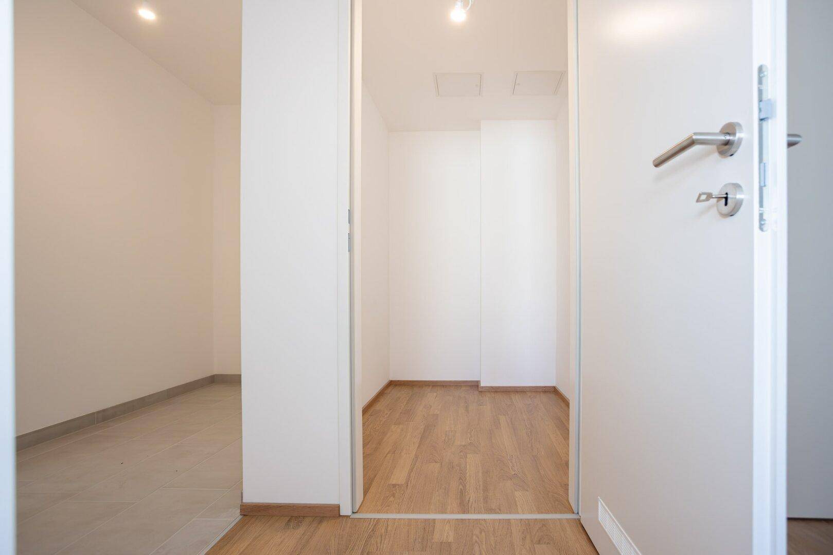 Kleiner, heller Abstellraum oder begehbarer Kleiderschrank mit Laminatboden und weißen Wänden.