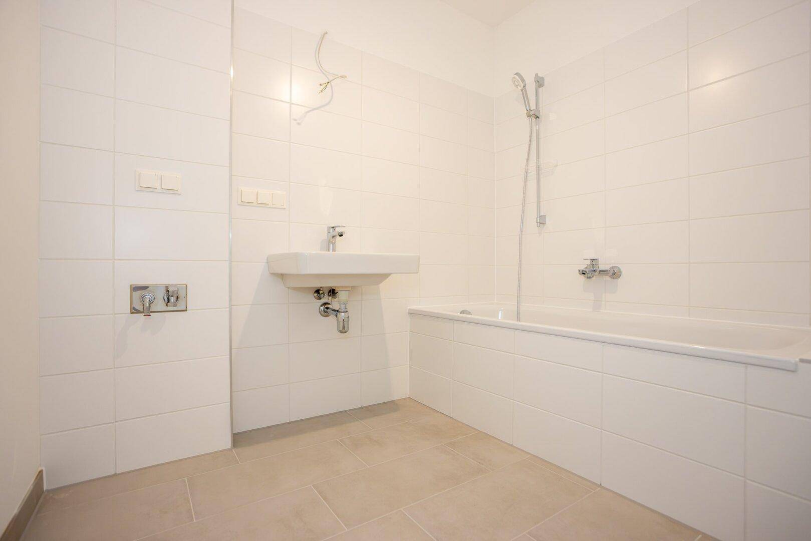 Modernes Badezimmer mit weißen Fliesen, Waschbecken und Badewanne mit integrierter Dusche.