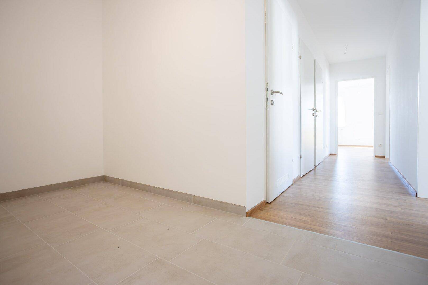 Heller Flur mit Übergang von Fliesen- zu Laminatboden und mehreren weißen Türen.