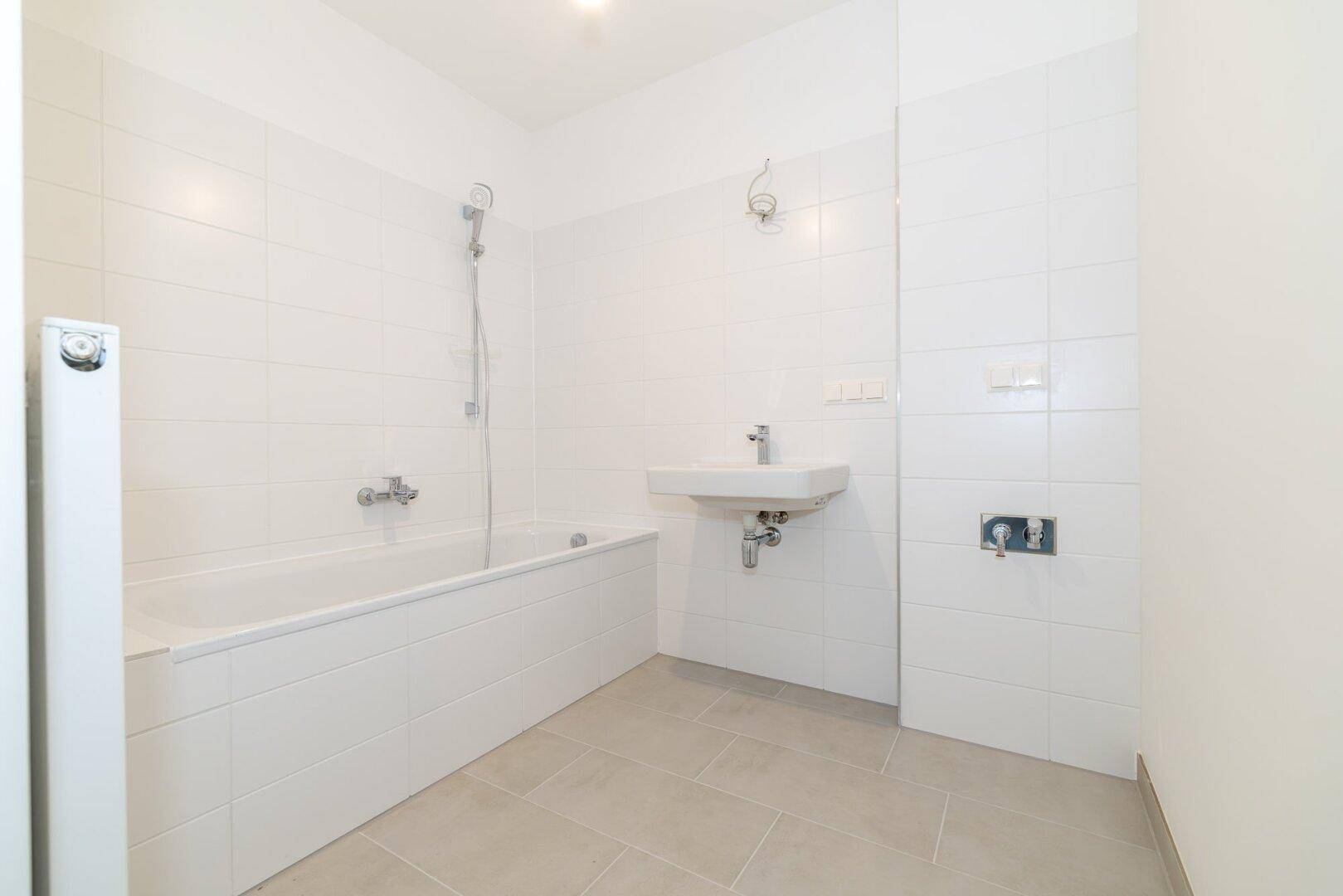 Modernes Badezimmer mit weißen Wandfliesen, grauen Bodenfliesen, Badewanne und Einzelwaschbecken.
