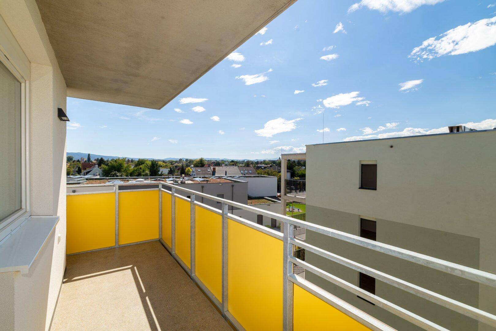 Heller Balkon mit gelben Sichtschutzelementen und Blick auf die umliegenden Gebäude und Landschaft.
