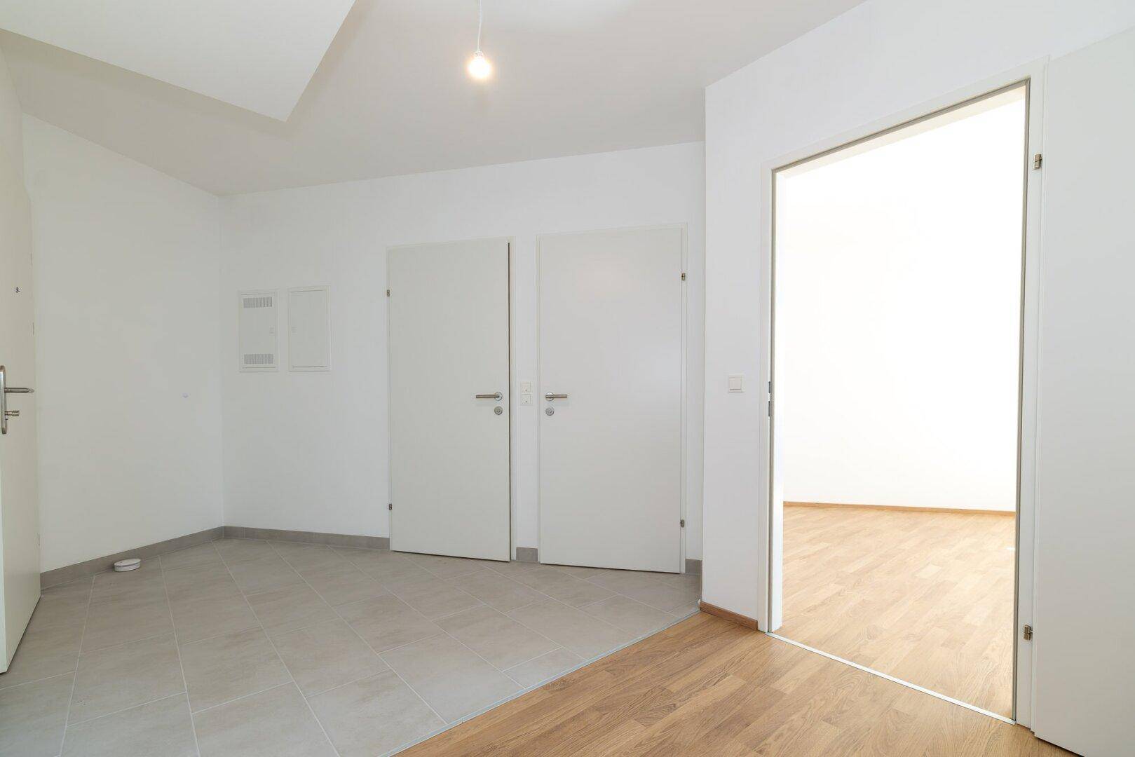 Geräumiger Flur mit Fliesenboden und Übergang zu Laminat, weißen Wänden und mehreren Türen.