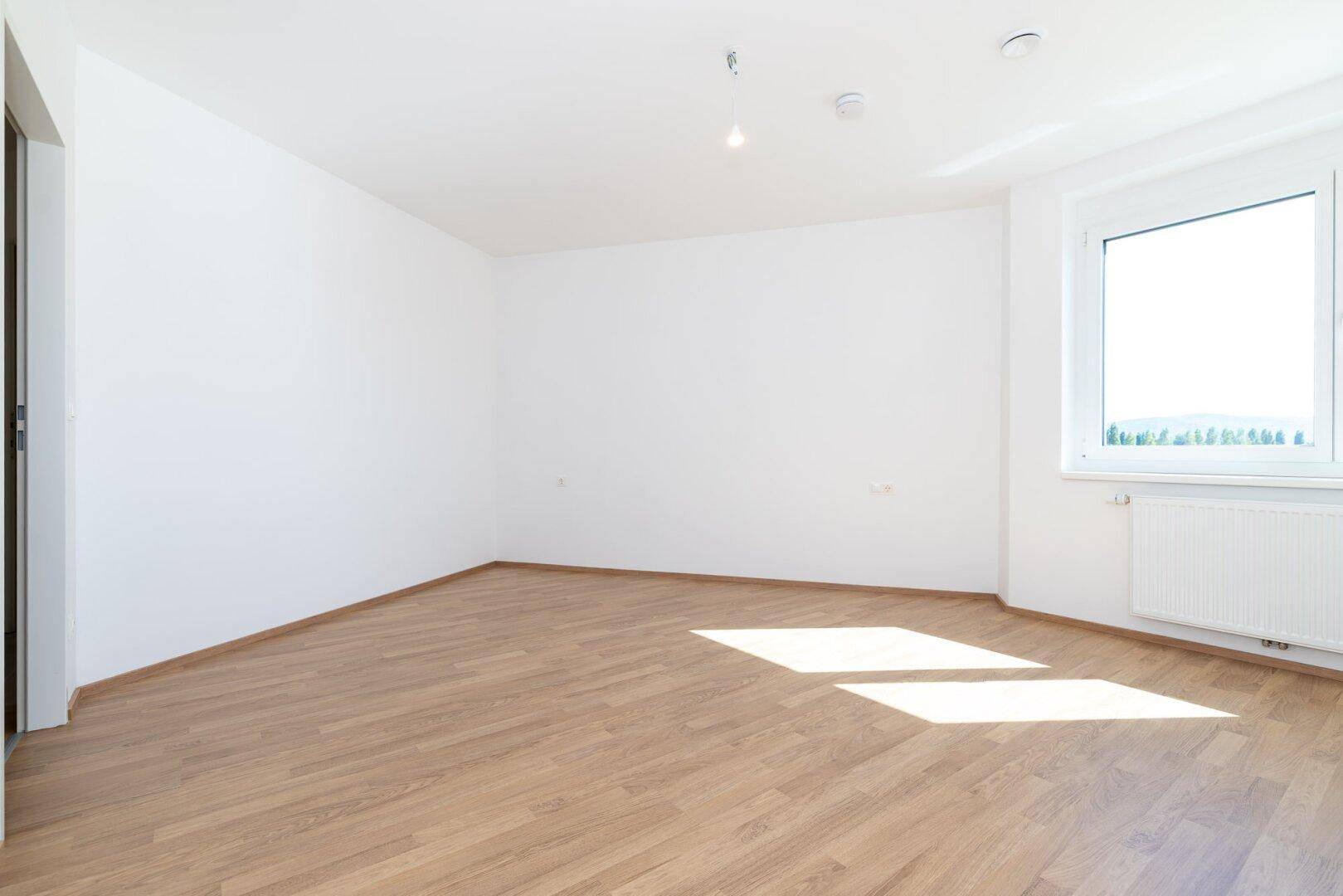 Geräumiges Schlafzimmer mit hellem Laminatboden, weißen Wänden und einem großen Fenster.
