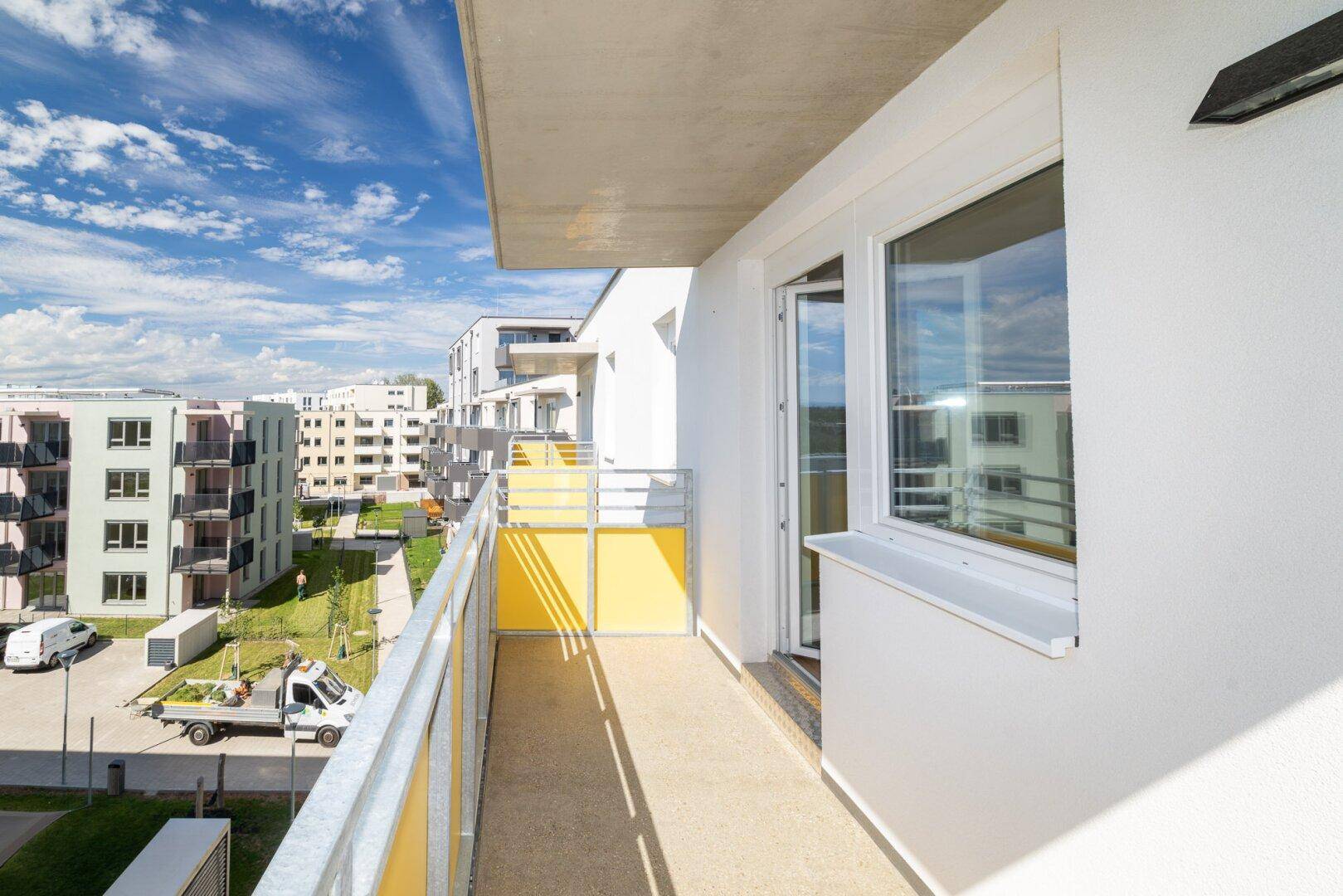 Langer Balkon mit gelben Sichtschutzelementen und Ausblick auf die Nachbarschaft und Parkplätze.
