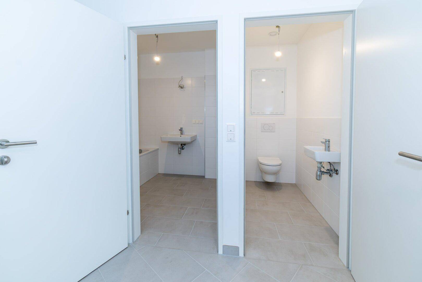 Blick in zwei separate Räume: ein Badezimmer mit Badewanne und ein Gäste-WC mit Toilette und Waschbecken.