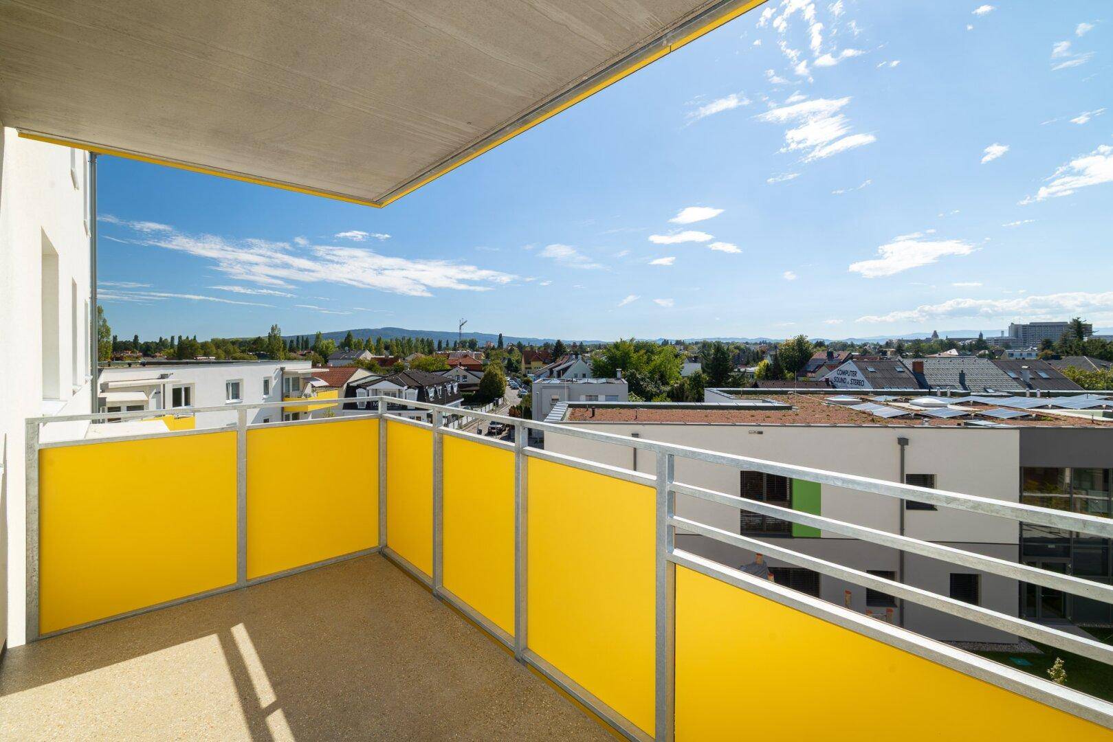 Sonniger Balkon mit gelben Brüstungselementen und Blick auf die Wohnsiedlung.