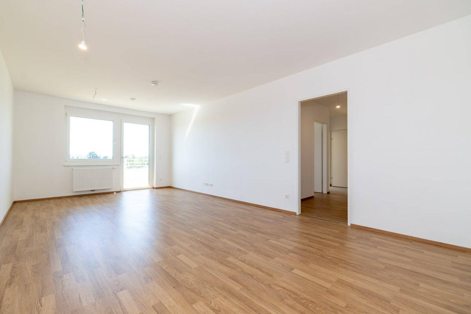 Geräumiges, leeres Zimmer mit Laminatboden und offenem Zugang zum Flur.