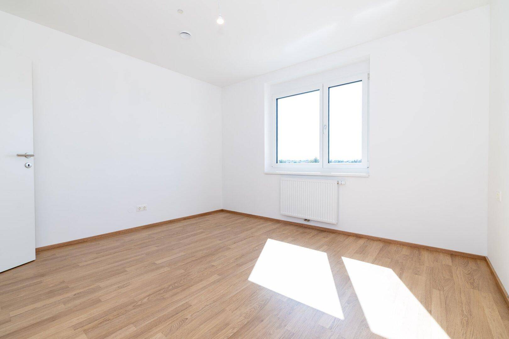 Lichtdurchflutetes Schlafzimmer mit Laminatboden und einem großen Fenster.