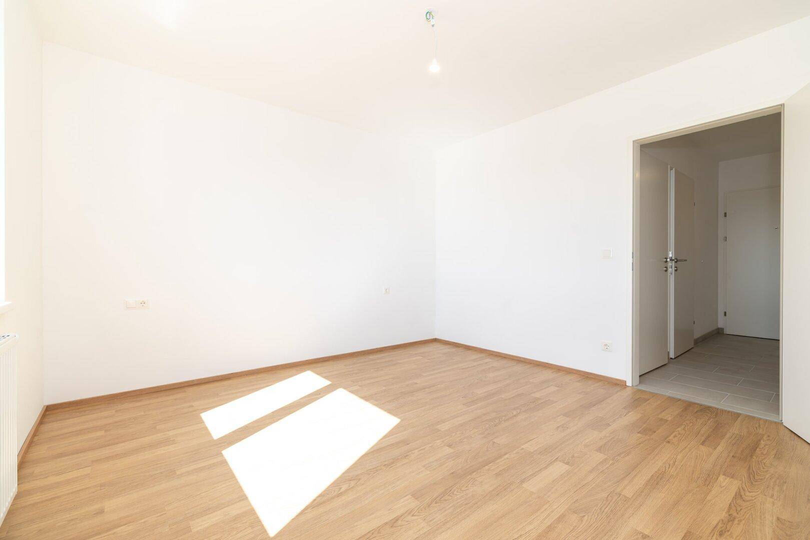 Helles Schlafzimmer mit Laminatboden und offenem Zugang zu einem weiteren Raum.