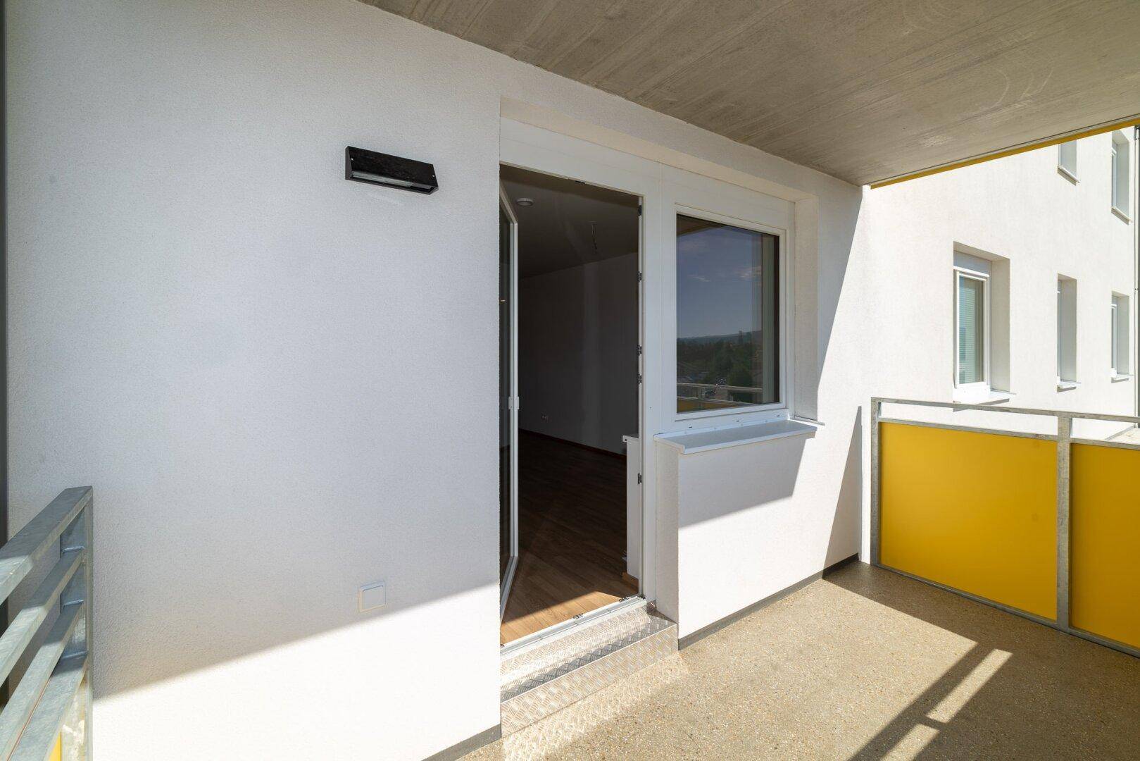 Überdachter Balkon mit Zugang zum Innenbereich und Blick auf die Fassade des Gebäudes.