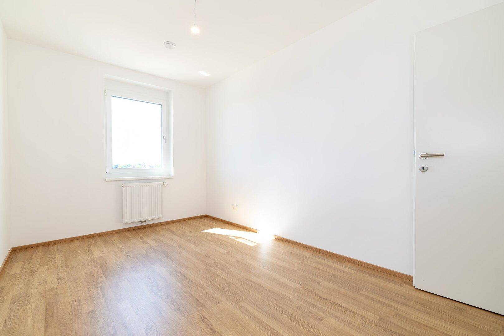 Lichtdurchflutetes Schlafzimmer mit Laminatboden und einem großen Fenster.
