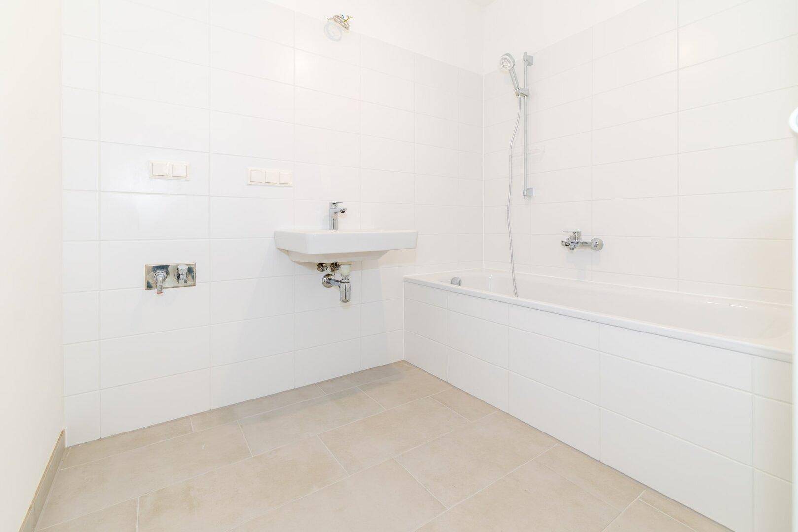 Modernes Badezimmer mit weißen Fliesen, Waschbecken und Badewanne mit Duschfunktion.