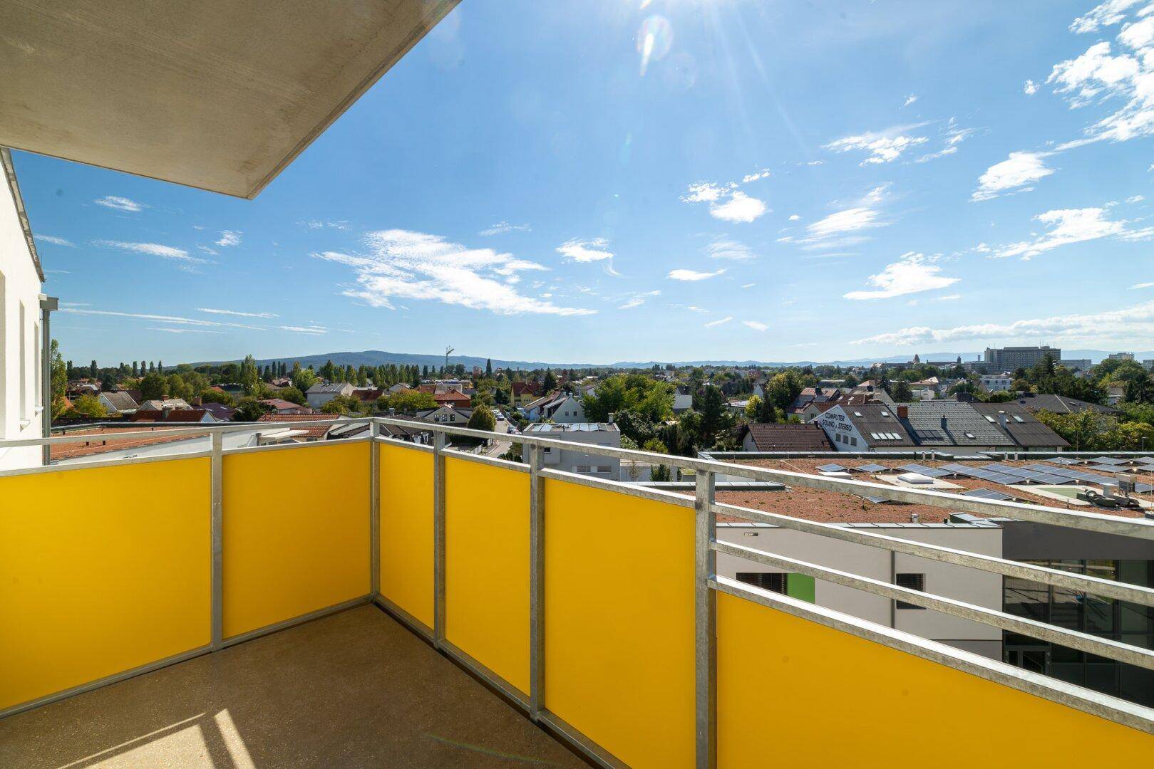 Heller Balkon mit gelben Sichtschutzwänden und Panoramablick über die Stadt und Berge.