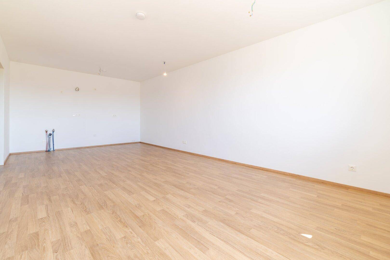 Heller, leerer Raum mit Laminatboden und weißen Wänden, bereit für die individuelle Gestaltung.