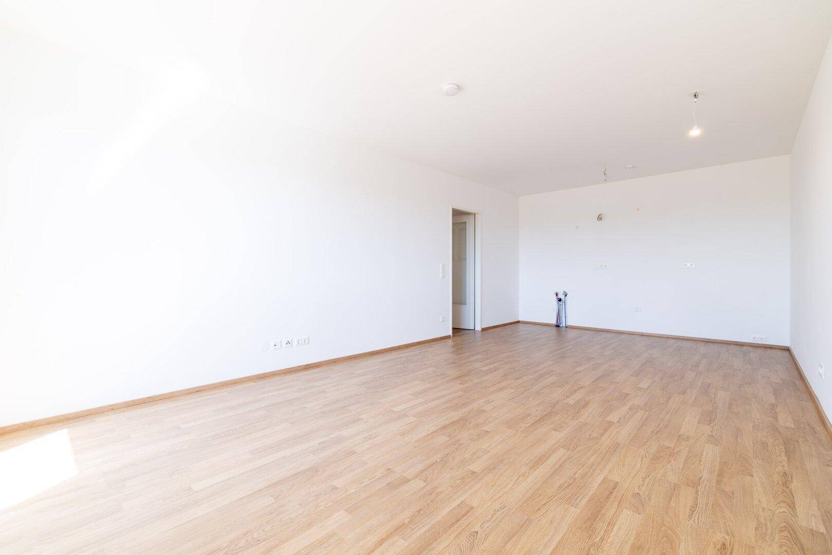 Geräumiger, heller Wohnbereich mit Laminatboden und Zugang zu weiteren Zimmern.