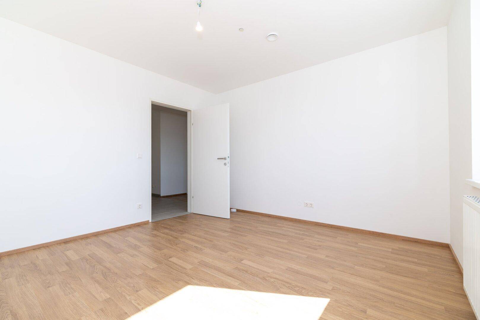 Geräumiges Schlafzimmer mit hellem Laminatboden und weiß gestrichenen Wänden.