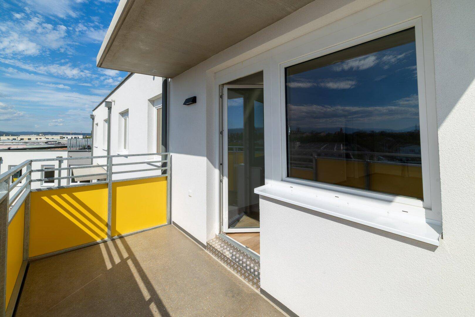 Heller Balkon mit gelben Akzenten und Zugang zum Innenbereich der Wohnung.