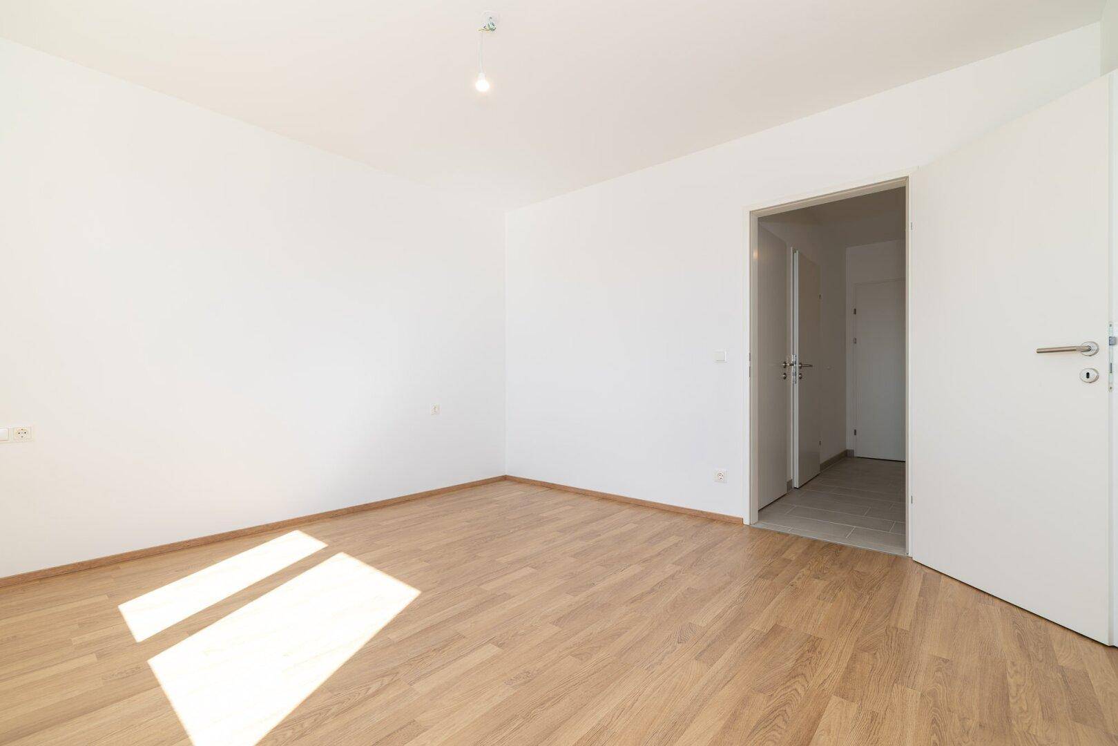 Lichtdurchflutetes Schlafzimmer mit Laminatboden und Zugang zum Flur.