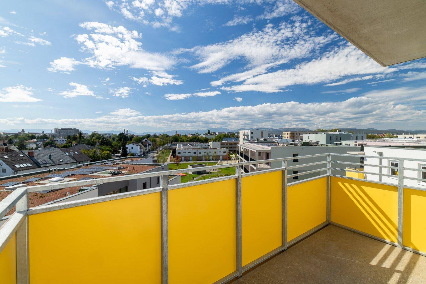 Sonniger Balkon mit gelben Brüstungselementen und weitem Blick über die Stadtlandschaft.