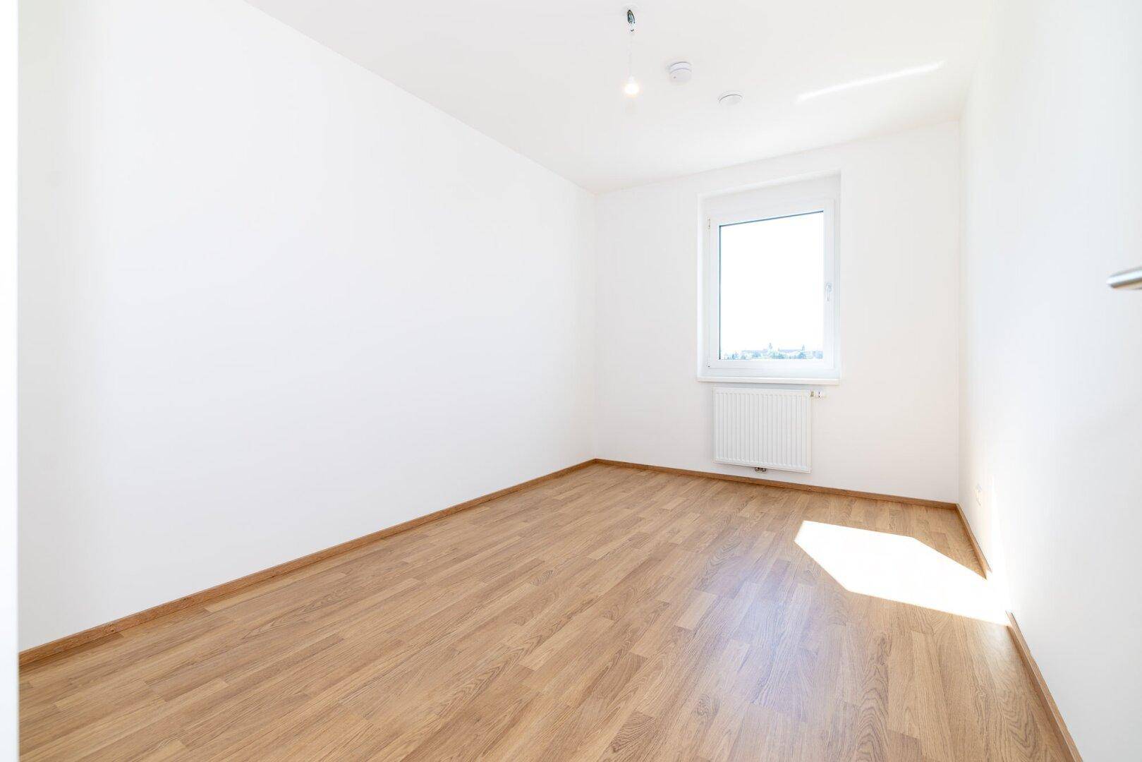 Helles Zimmer mit Laminatboden und Fenster, ideal als Schlaf- oder Arbeitszimmer.