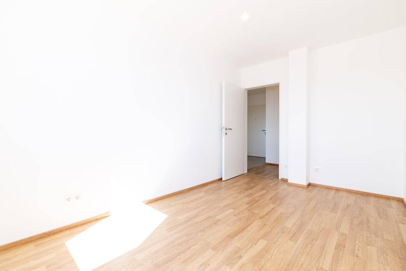 Geräumiges Zimmer mit Laminatboden und weiß gestrichenen Wänden, bereit zur Einrichtung.