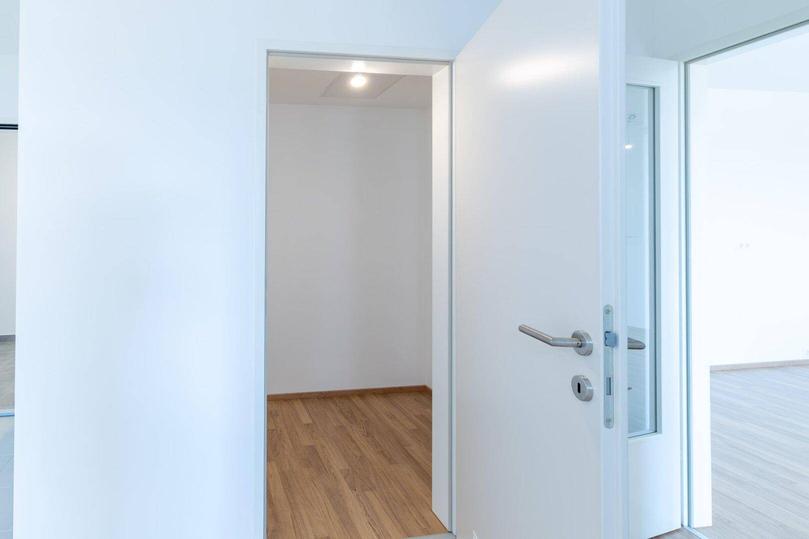 Offene Tür führt in einen weiteren hellen Raum mit Laminatboden.