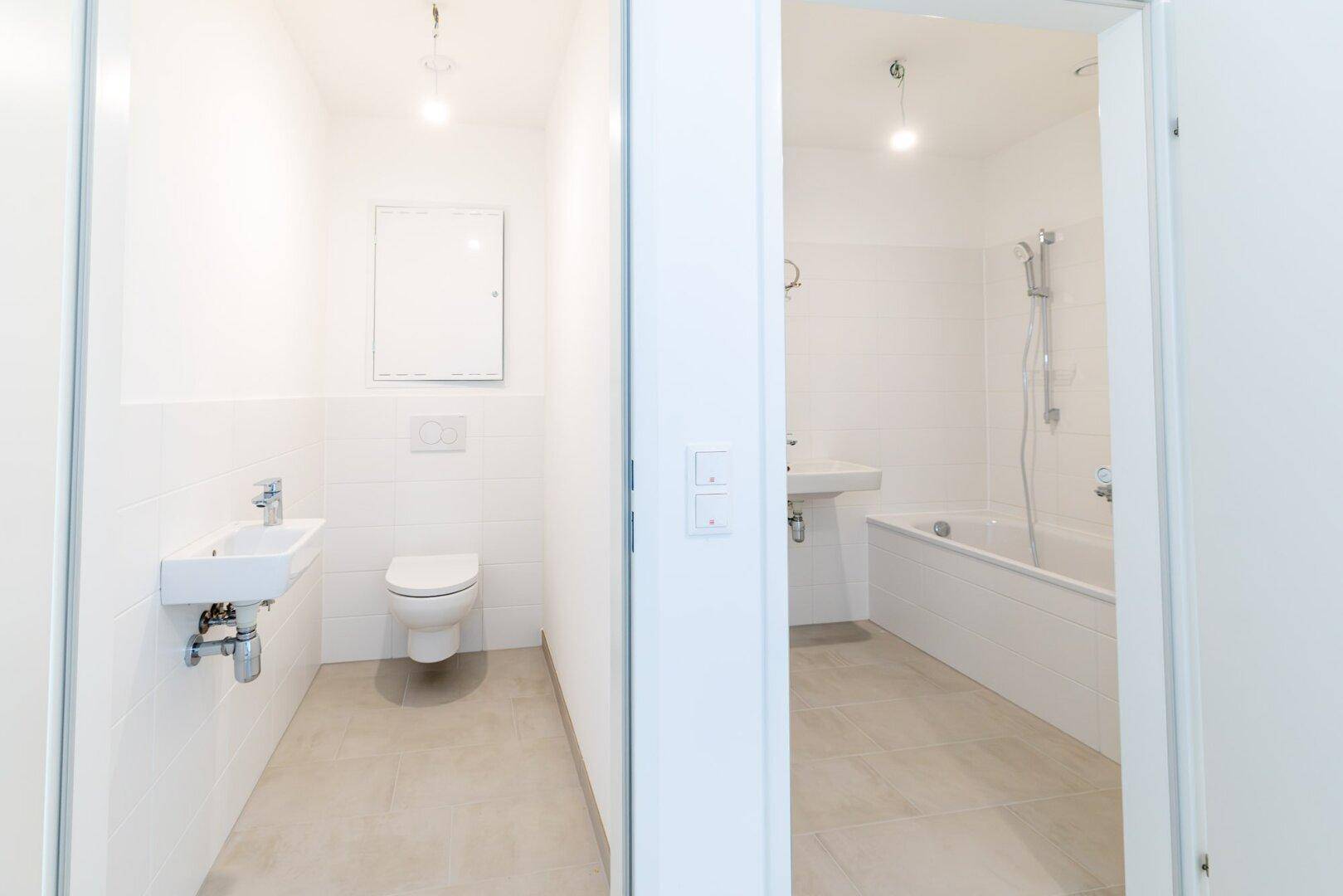 Blick in zwei separate Badezimmer: ein Gäste-WC und ein Hauptbad mit Badewanne.