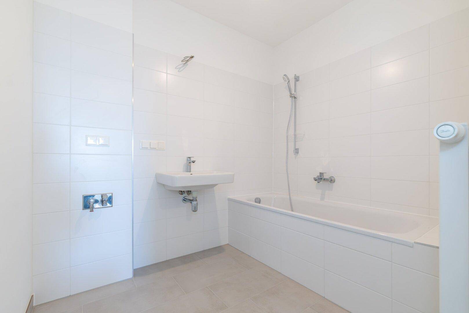 Modernes Badezimmer mit weißen Fliesen, Badewanne, Waschbecken und Duscharmatur.